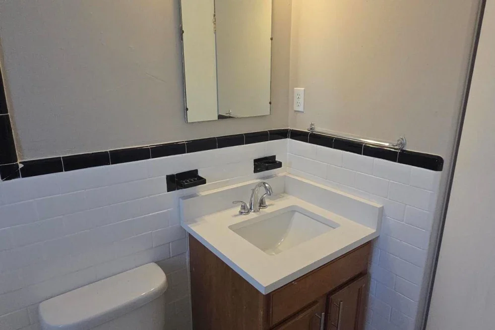 Bathroom sink with wooden cabinet, mirror, and tile walls.