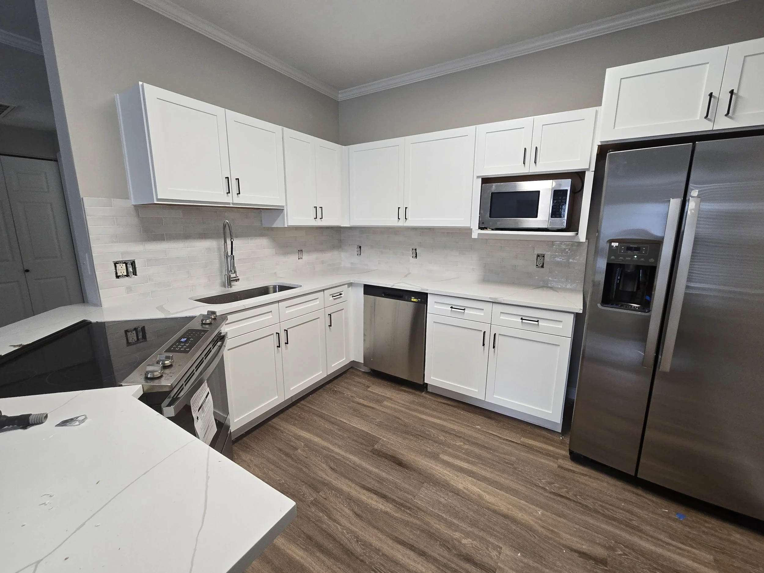 Modern kitchen with white cabinets, stainless steel appliances, gray backsplash, and wood-look flooring.