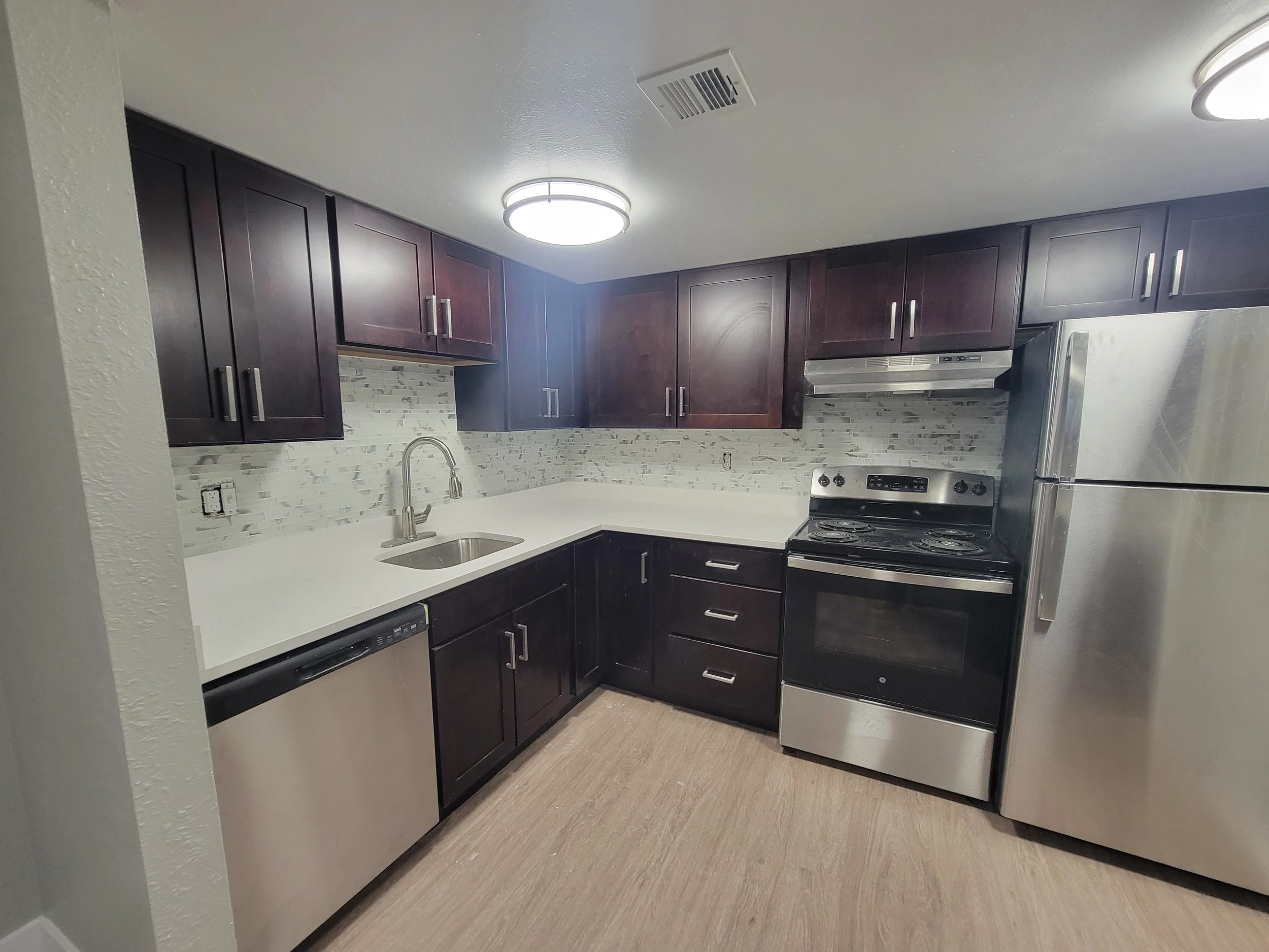 Modern kitchen with dark wood cabinets, stainless steel appliances, a white countertop, a mosaic backsplash, and a ceiling light fixture.