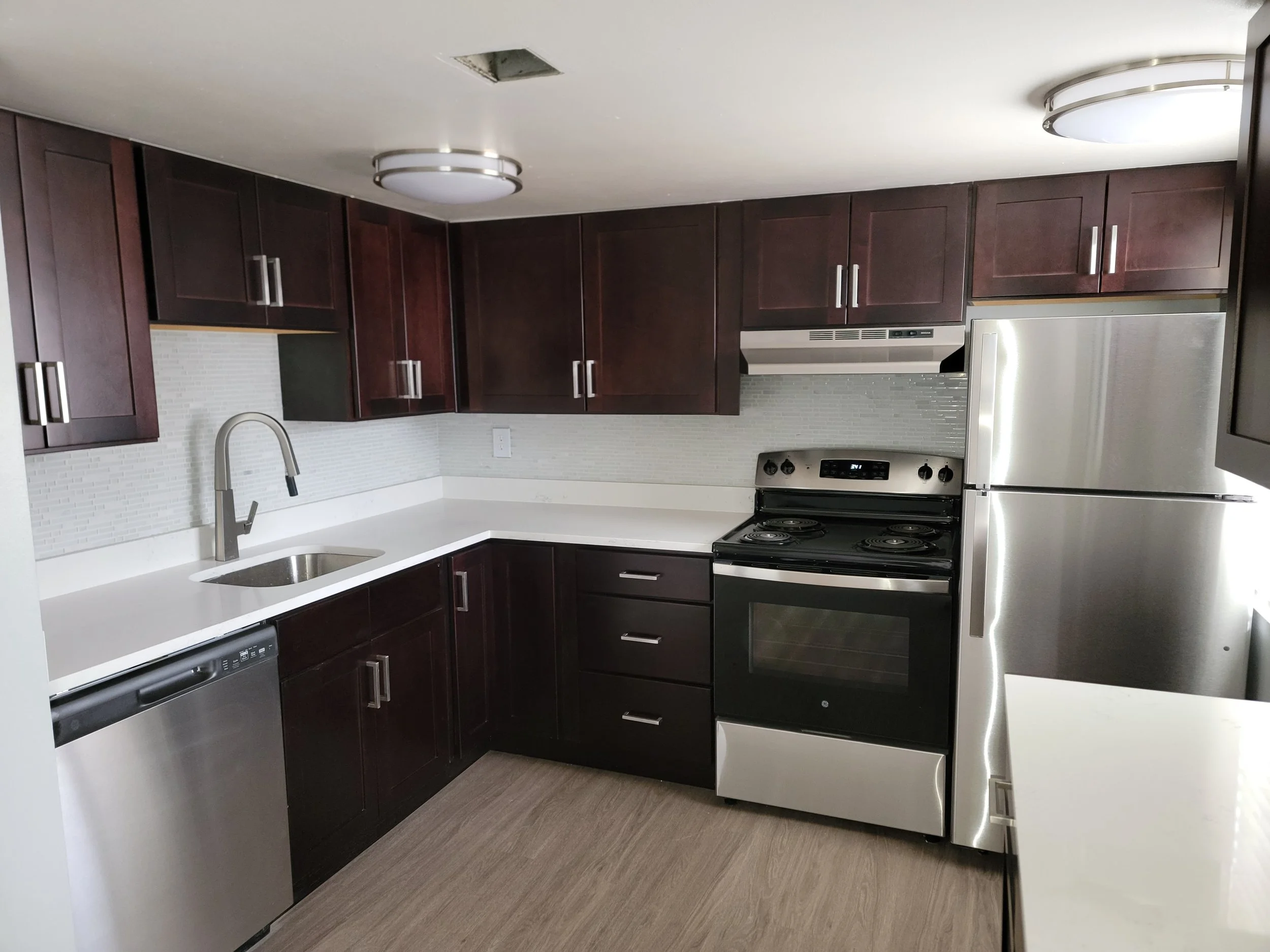 Modern kitchen with dark wooden cabinets, stainless steel appliances, a white countertop, and a textured backsplash.