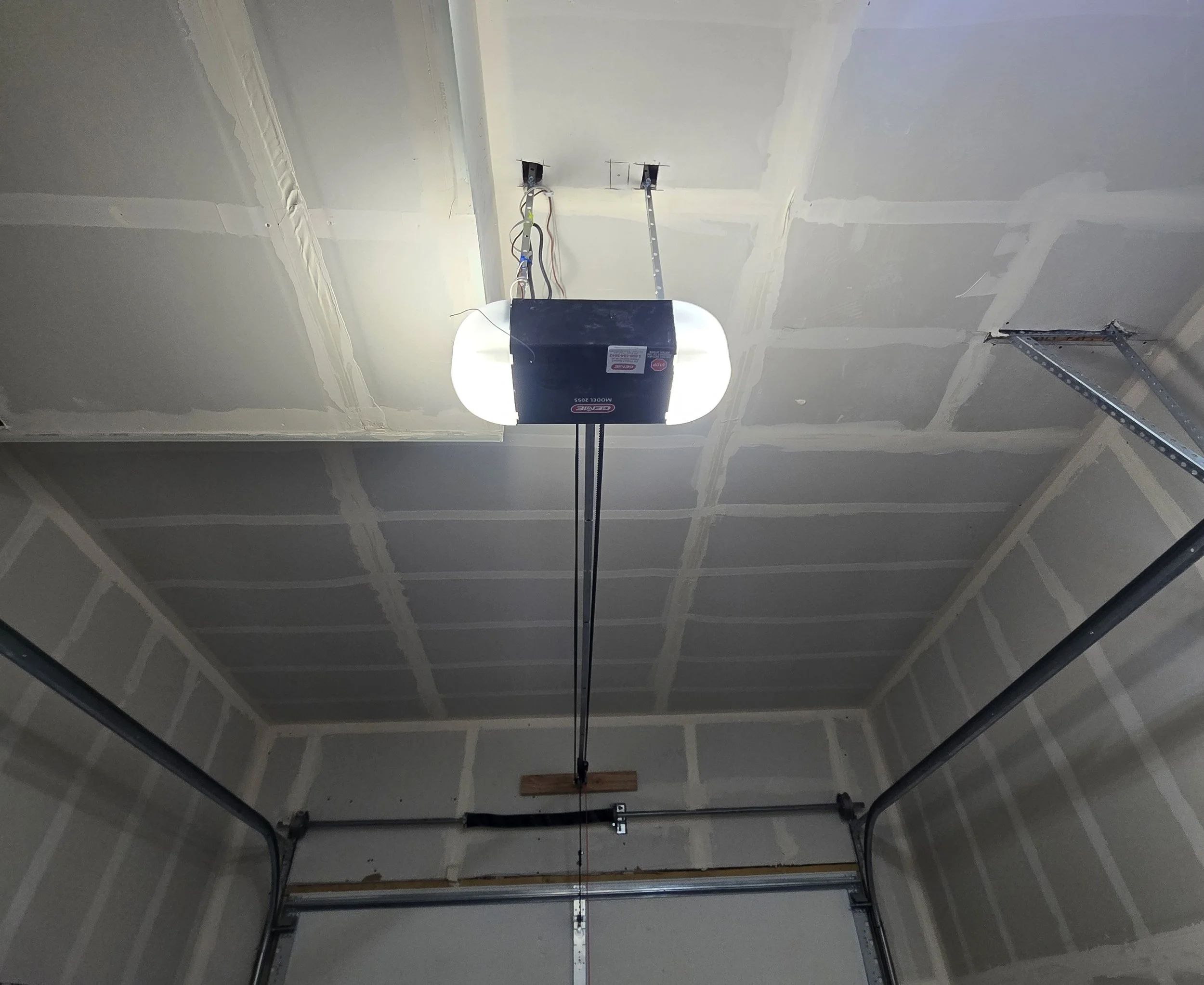 Garage door with an automatic opener, visible tracks, and partially finished drywall ceiling.