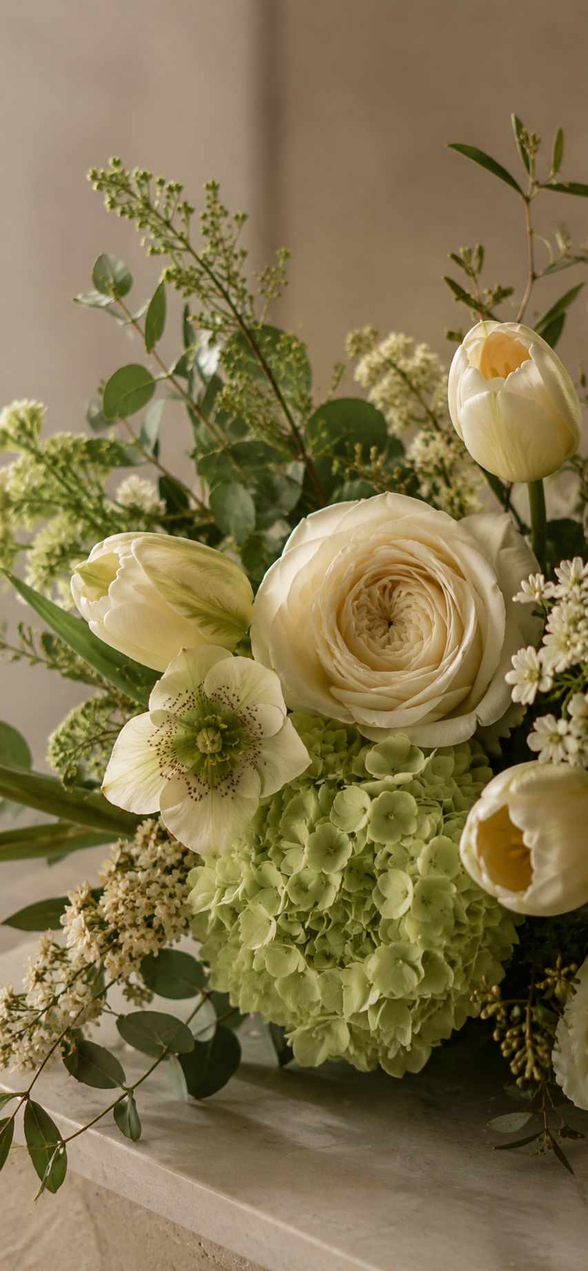 A bouquet of cream-colored roses, tulips, hydrangeas, and greenery on a neutral background.
