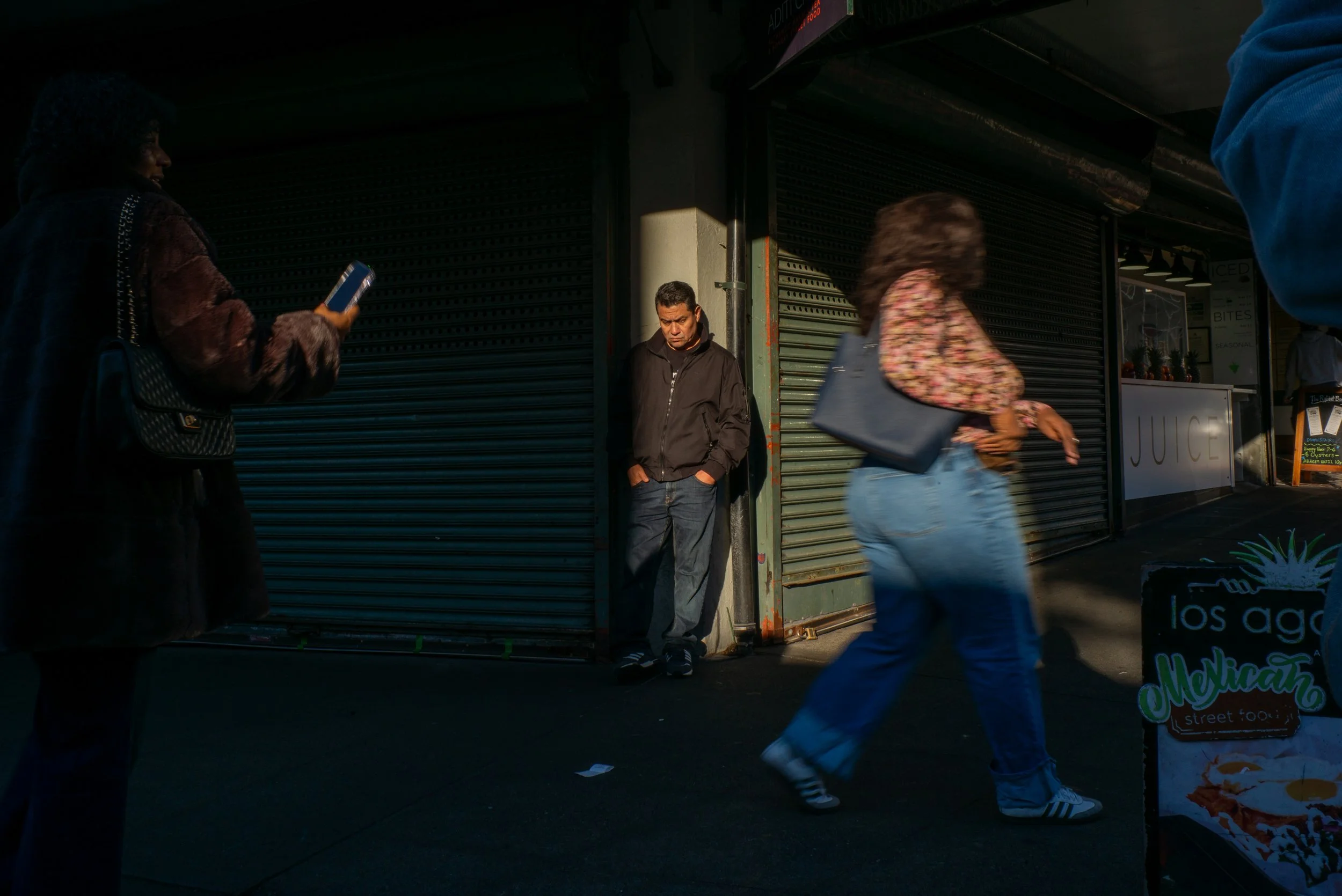 People walking by a closed storefront with shutter doors on a city street.