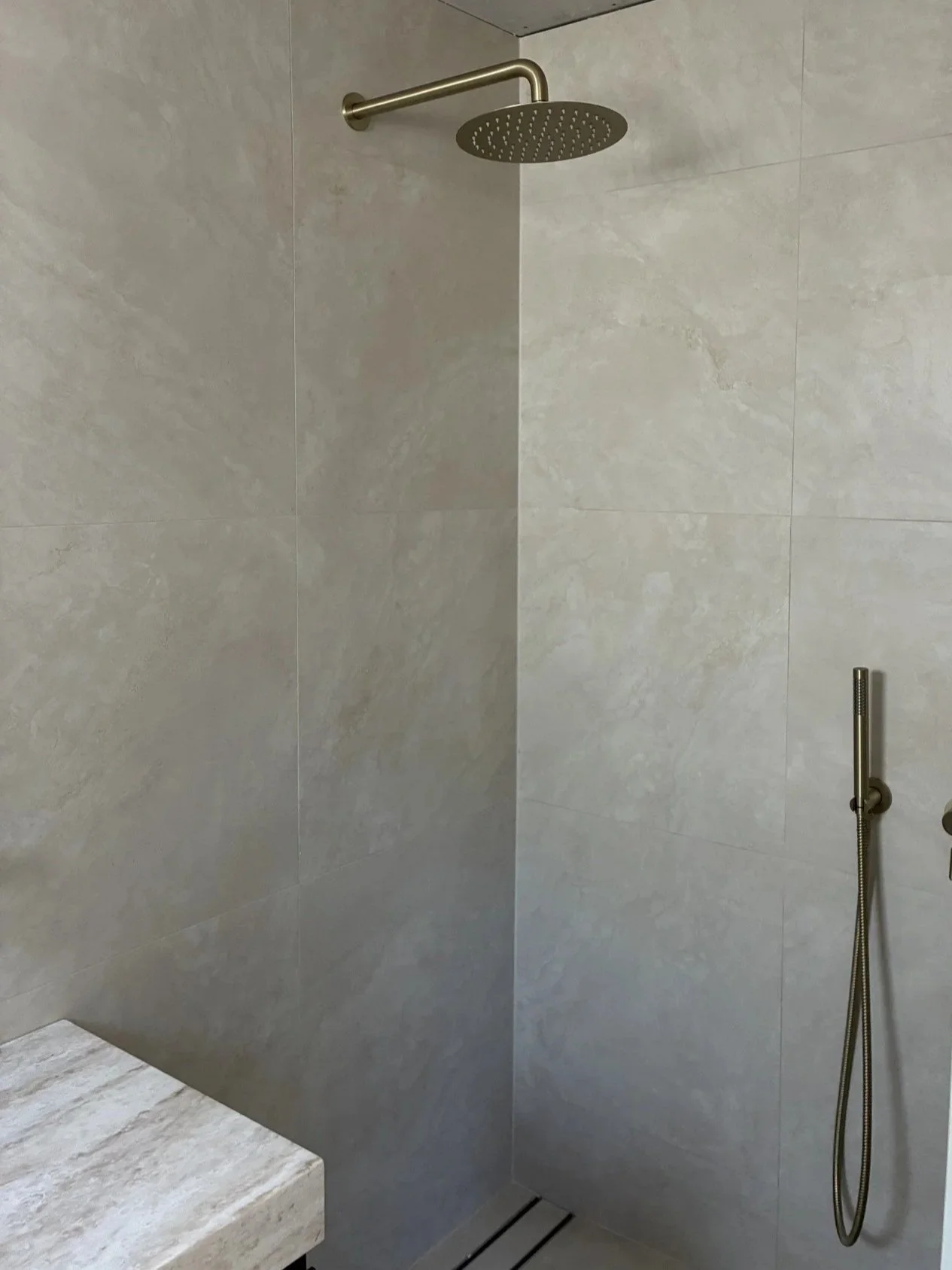 Modern bathroom renovation fit-out completed by Crums Plumbs, featuring a rain shower and handheld shower on beige tiled walls.