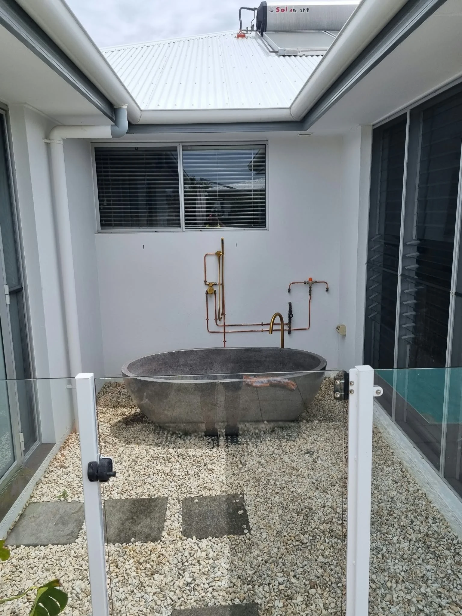 Outdoor bath plumbing installation with exposed hot and cold water pipework.