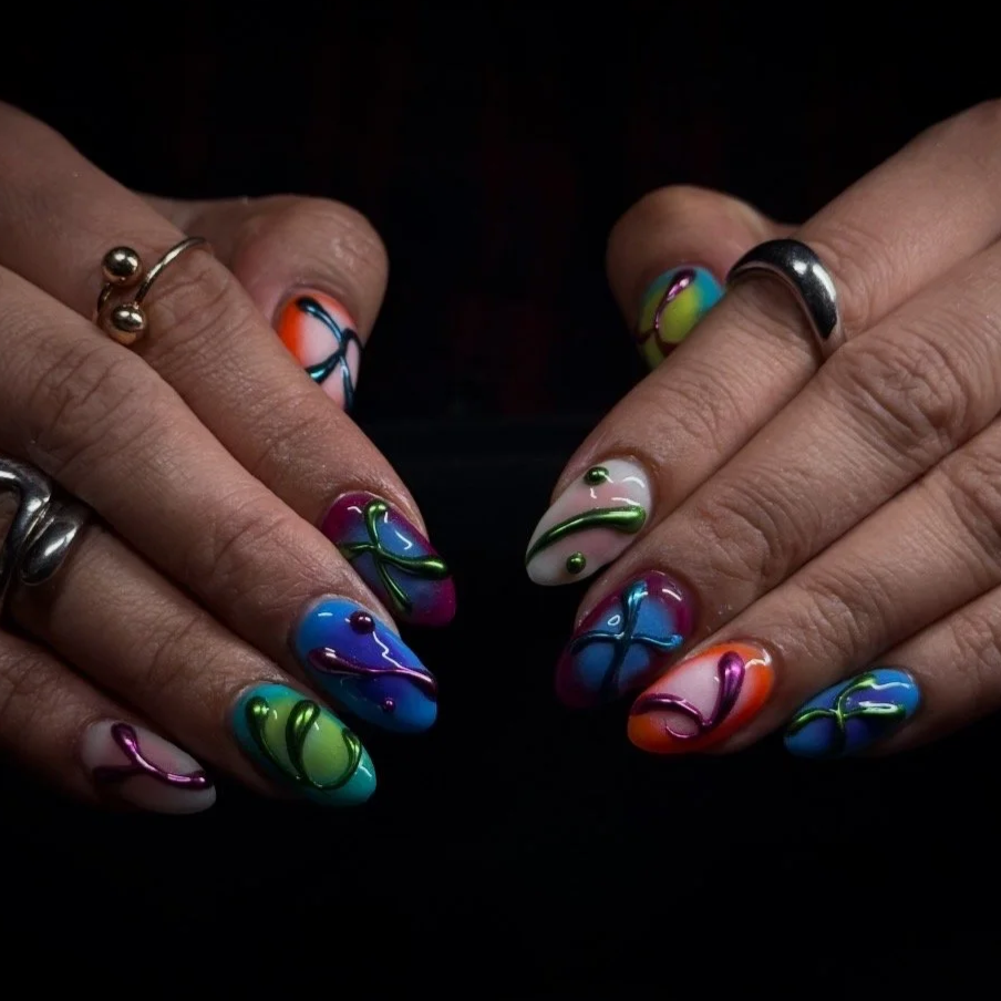 Close-up of hands with colorful rainbow swirl nail art and rings, set against a black background.
