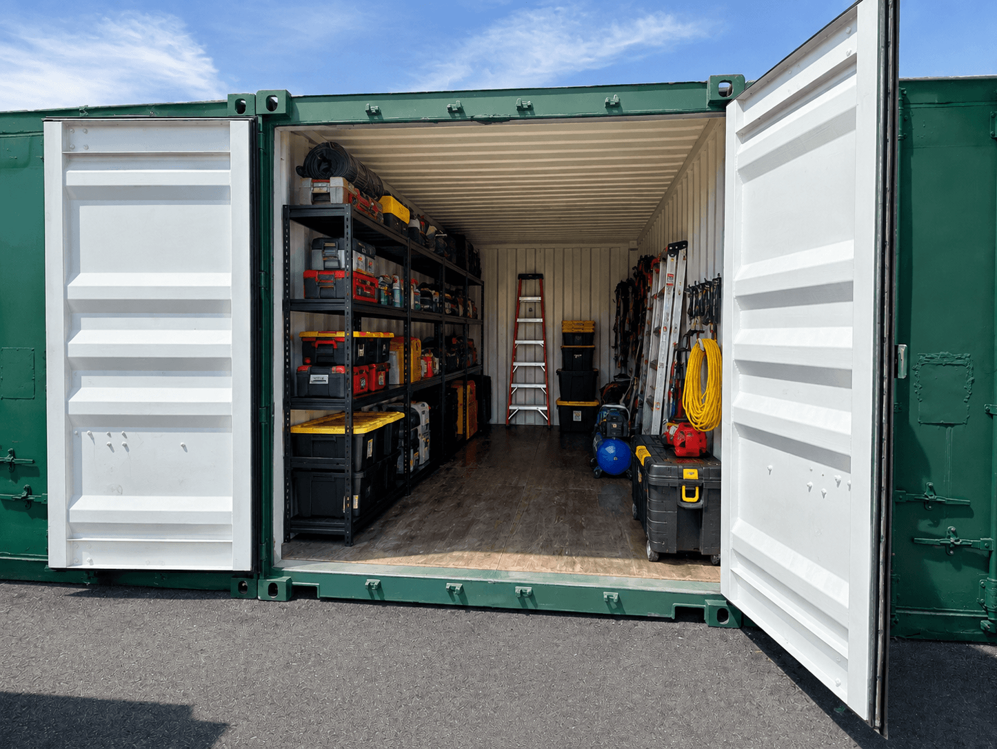 Interior of a storage container with shelves holding various power tools and equipment, ladder, yellow extension cord, and a blue air compressor.