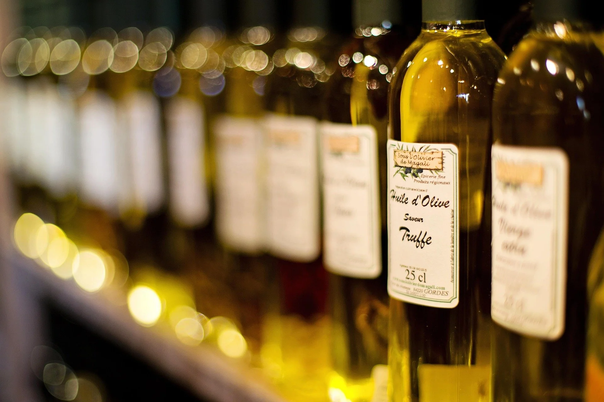 Line of olive oil bottles on a store shelf with blurred yellow and white lights in the background.