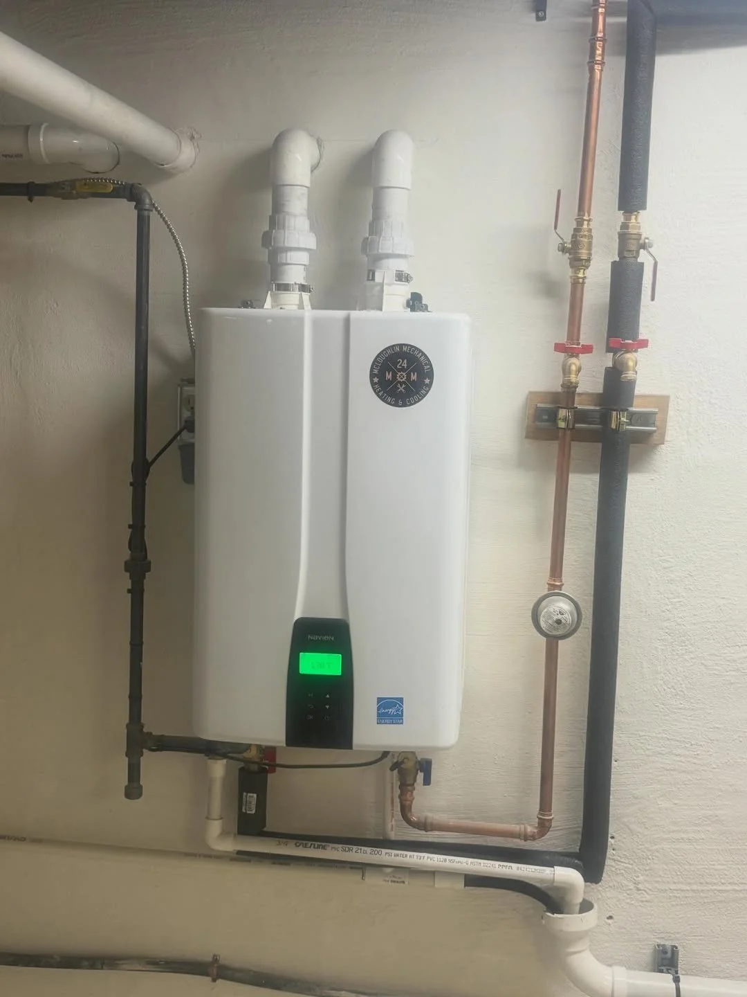 A wall-mounted tankless water heater with pipes and gauges.