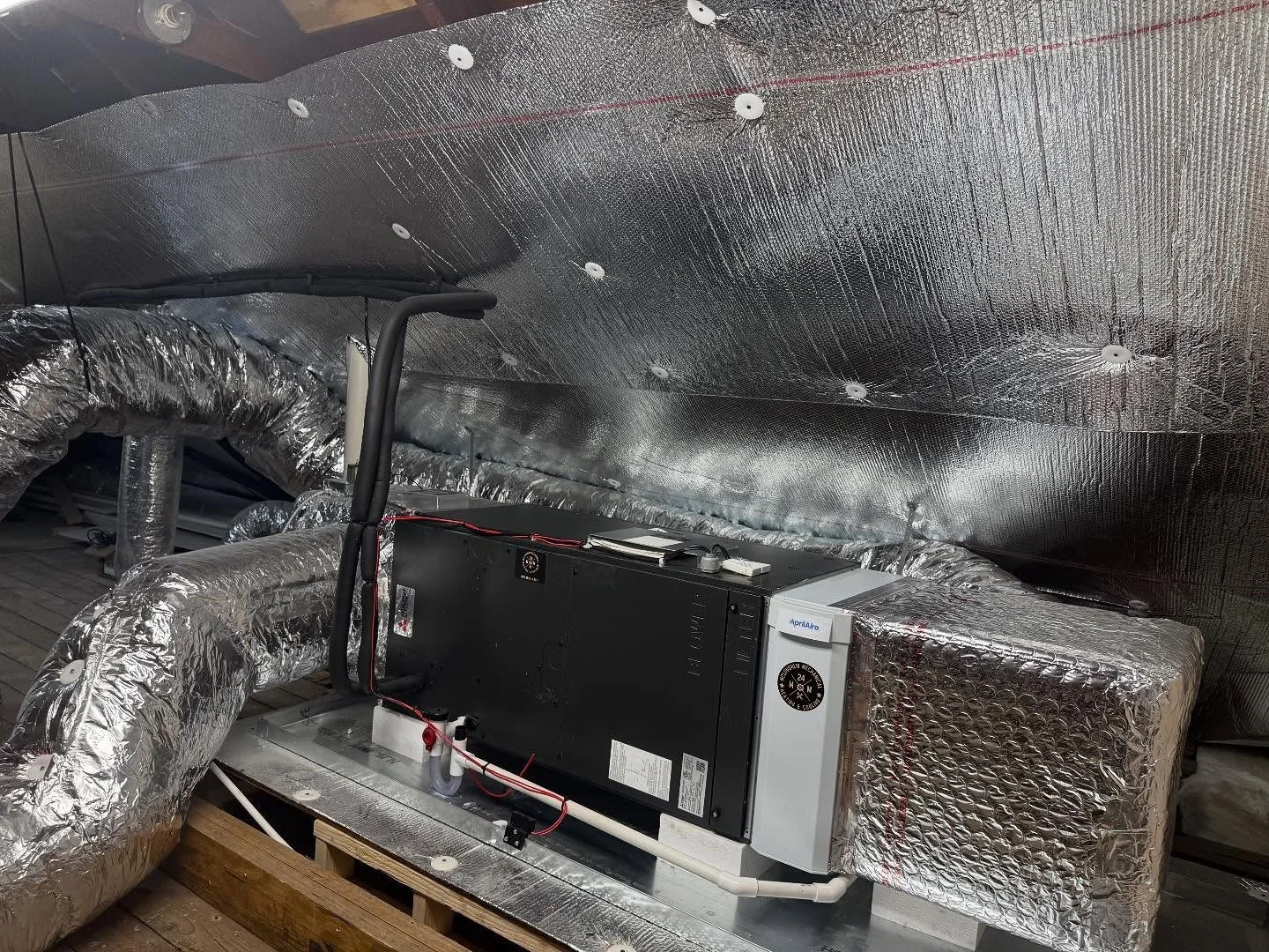 HVAC system equipment installed in an attic space, with insulated ductwork and a black air handling unit.