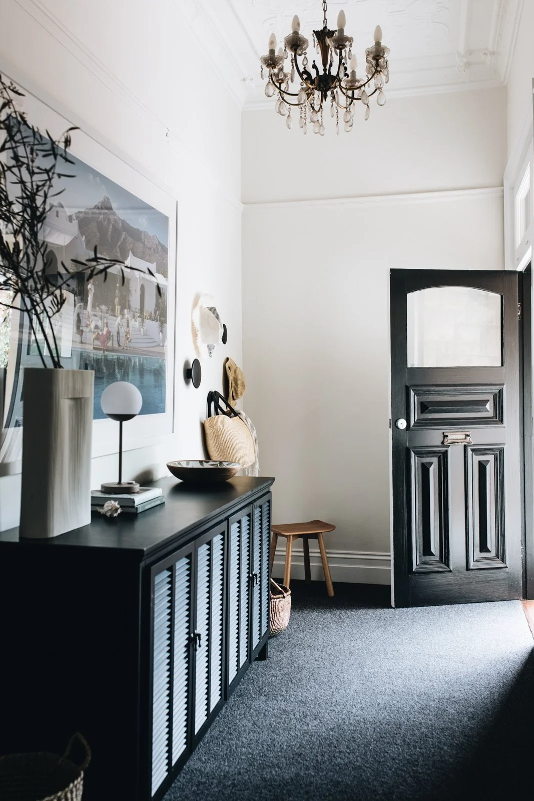 Entryway with black door, black sideboard, framed picture, chandelier, and decorative items.