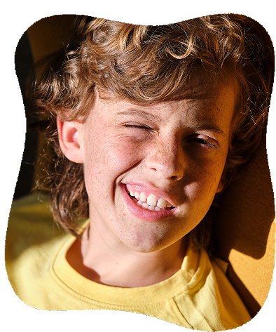 A young boy with curly hair making a funny face with one eye closed and sticking out his tongue.