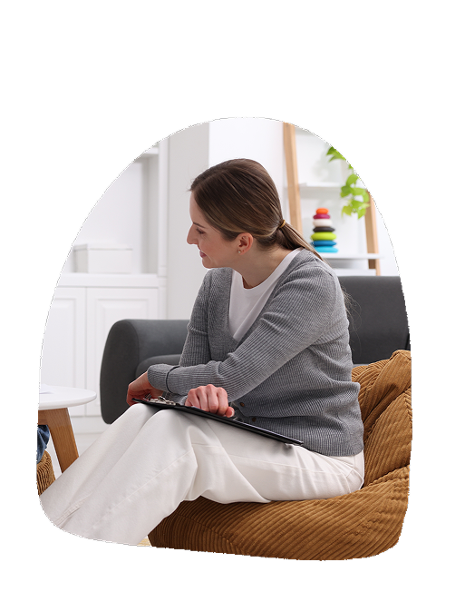 Woman sitting on a brown sofa using a tablet with white walls and shelves in the background.