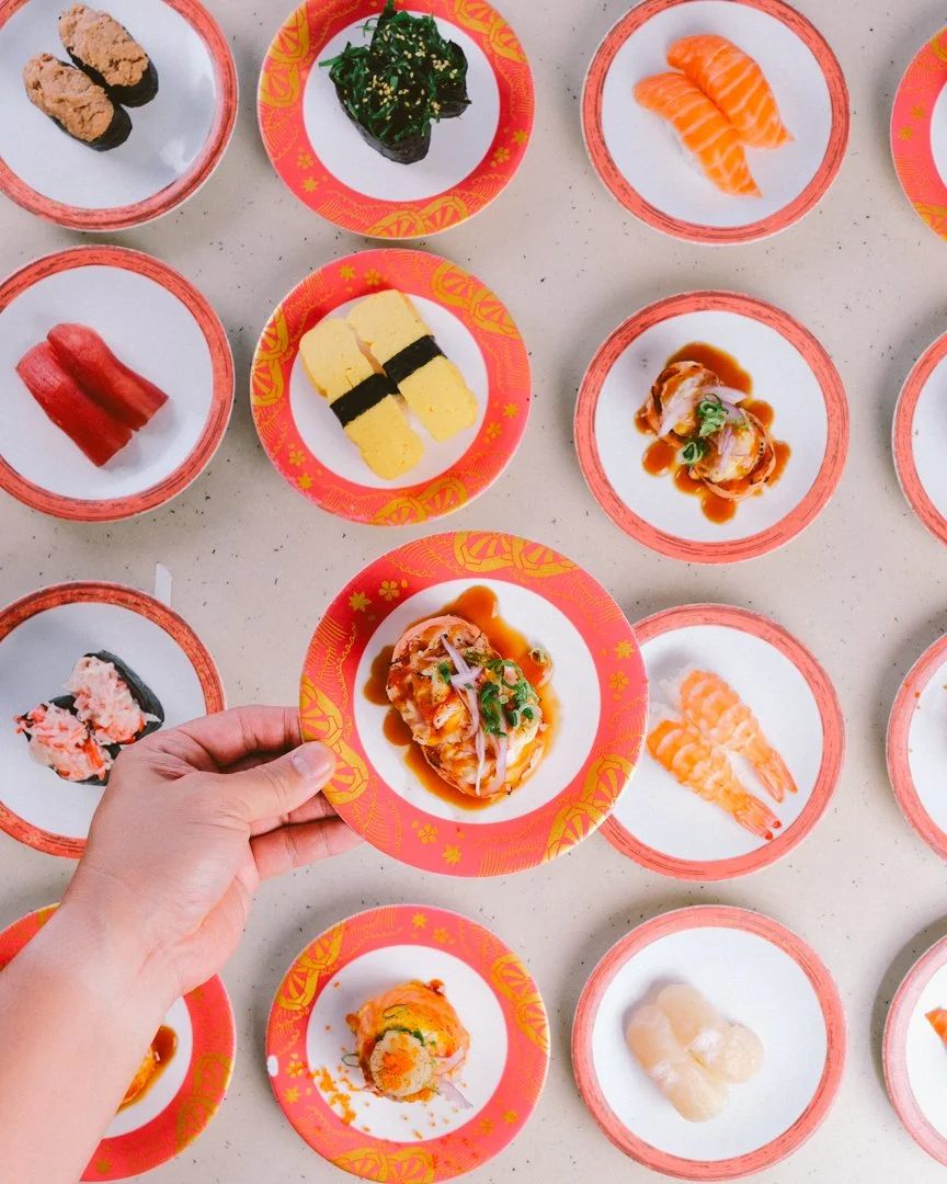 Small plates with various types of sushi, including nigiri and sashimi, on a light-colored surface.