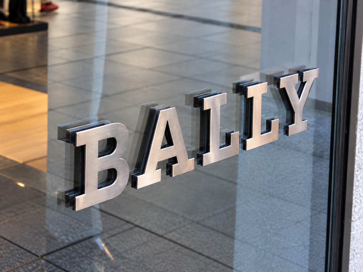 Close-up of a glass door with the word 'BAILLY' in metallic letters, showing an indoor setting with tile flooring visible through the glass.