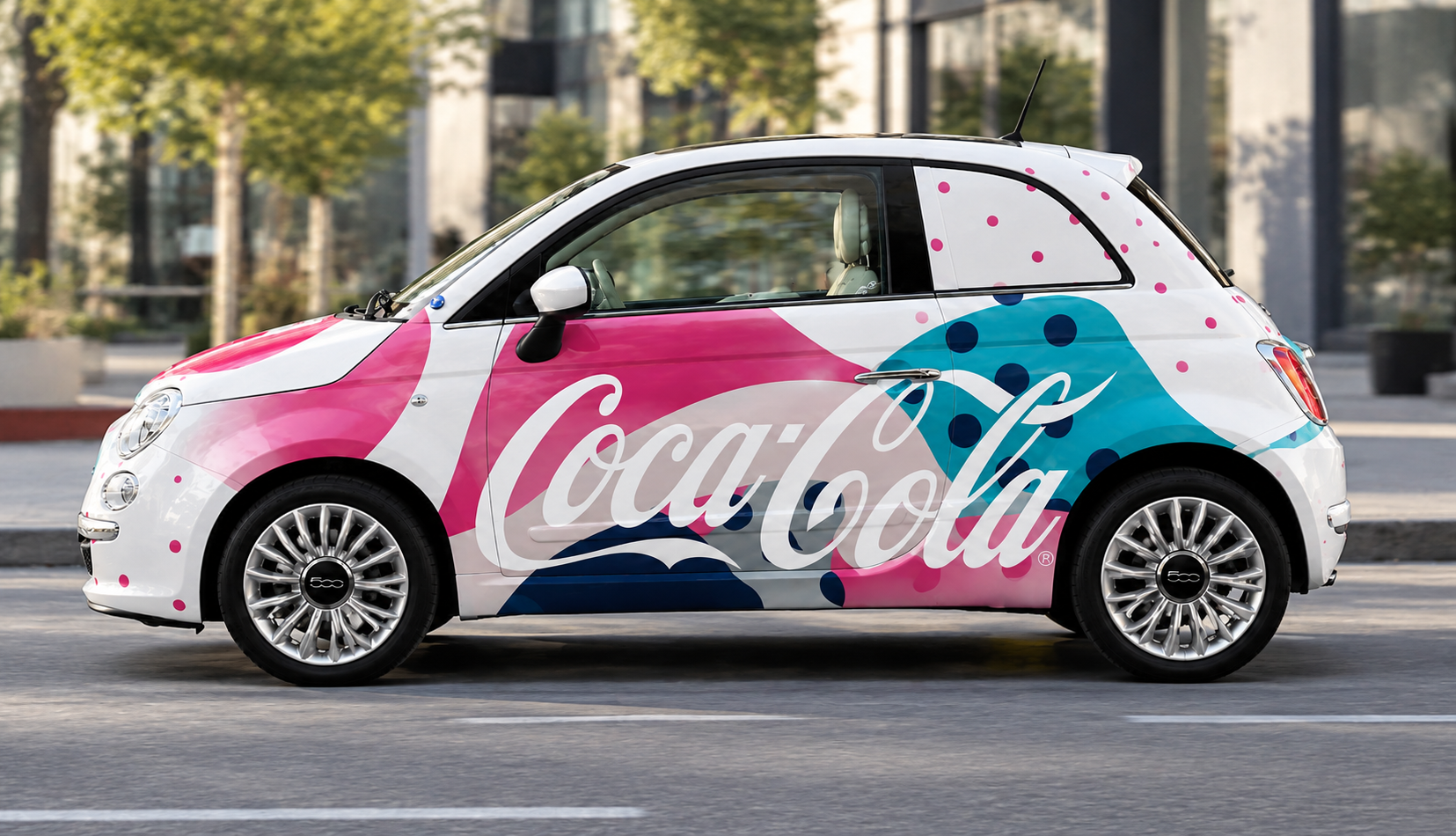 A Fiat 500 car with a colorful Coca-Cola wrap design featuring pink, blue, and white bubbles and the Coca-Cola logo, driving on a city street.