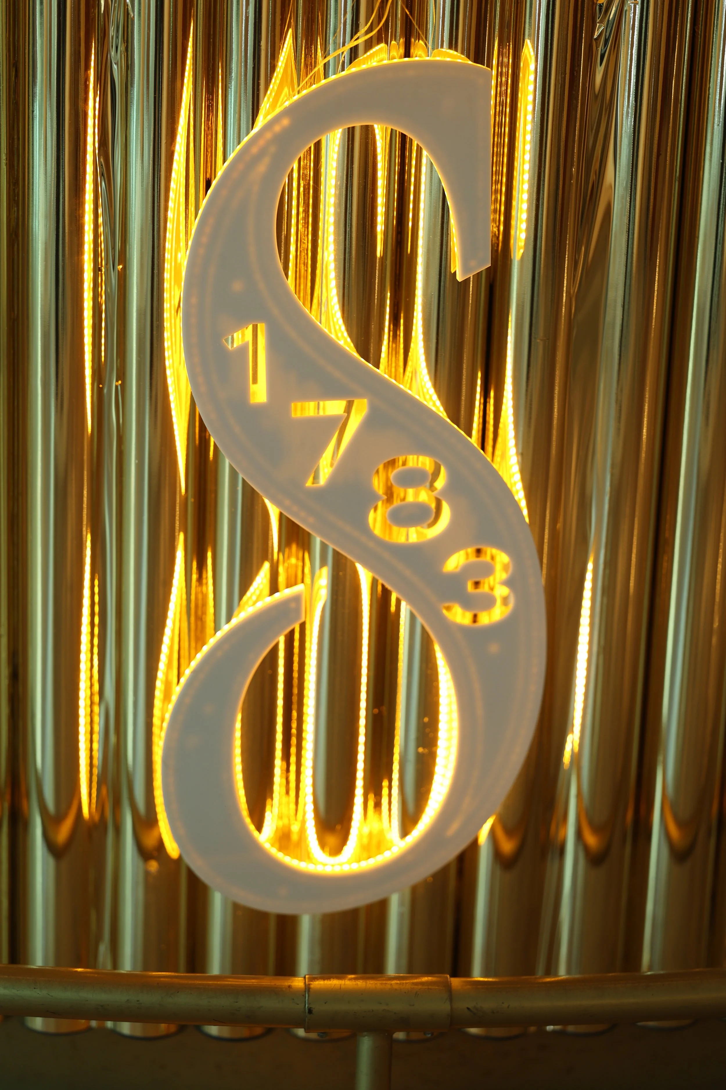 Close-up of a glowing neon sign with a large, illuminated musical note symbol against a backdrop of reflective metallic strips.