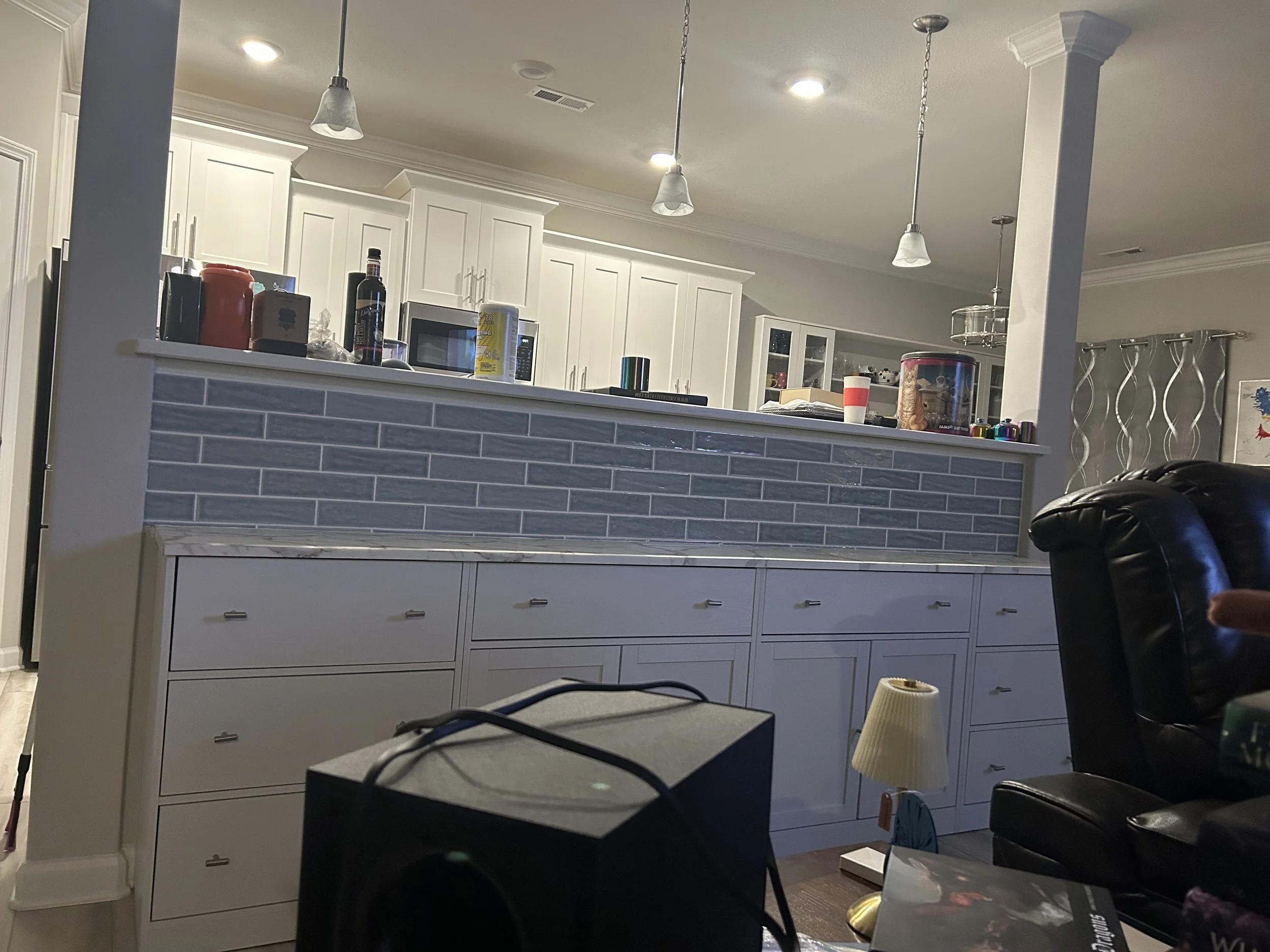 Modern kitchen with white cabinets, blue-gray tile backsplash, and pendant lighting.