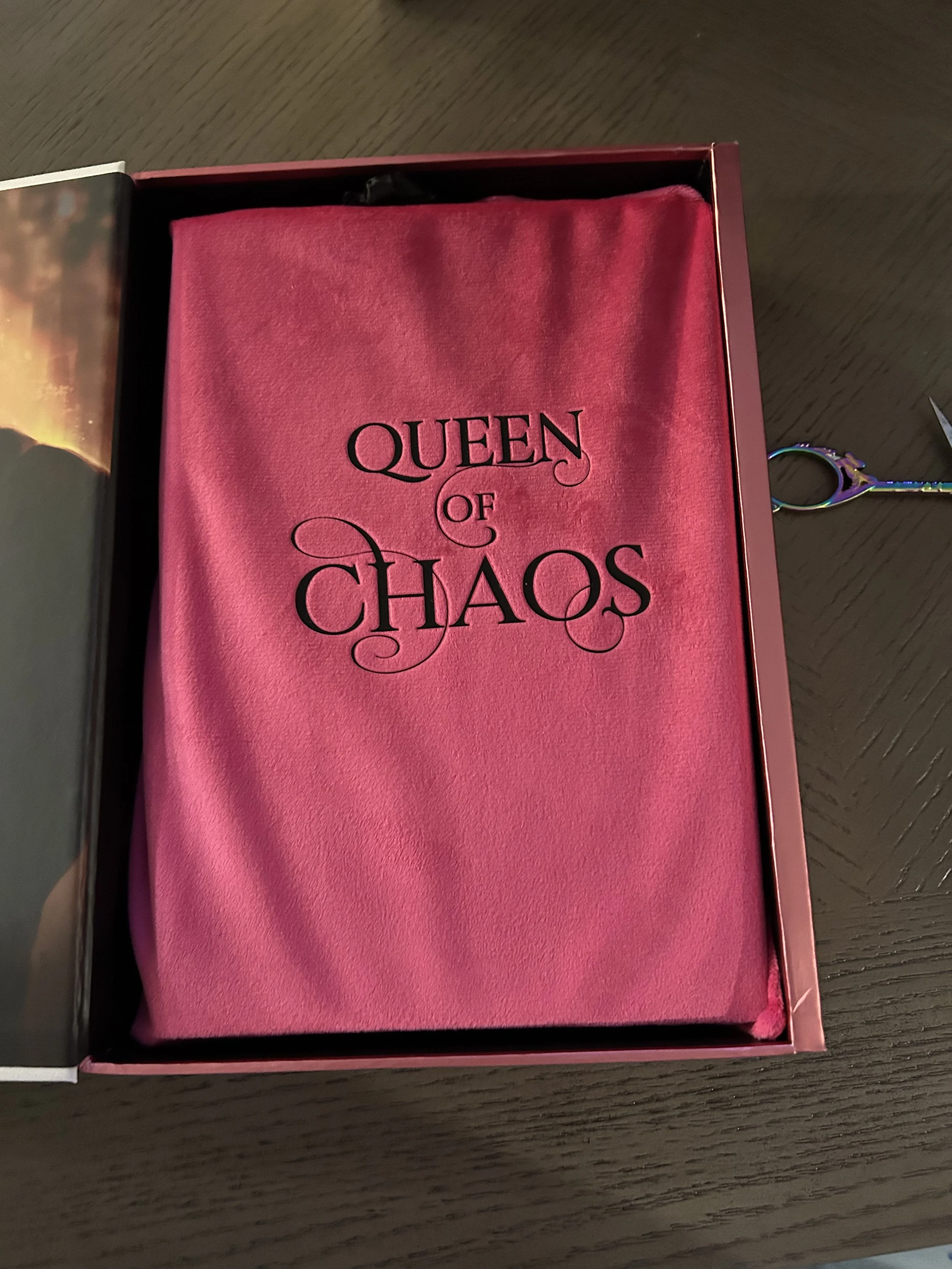 Hot-pink velvet Queen of Chaos book bag embroidered with the title inside a black presentation box.