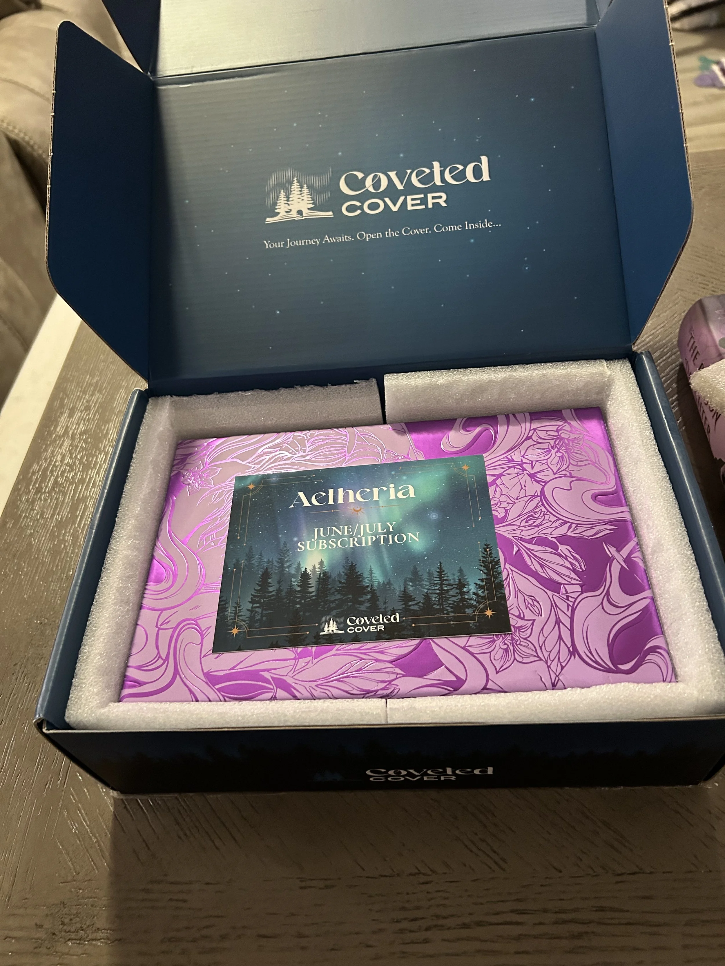 Open Coveted Cover collector's box revealing a metallic-purple illustrated slipcase and an Aetheria June/July subscription card.