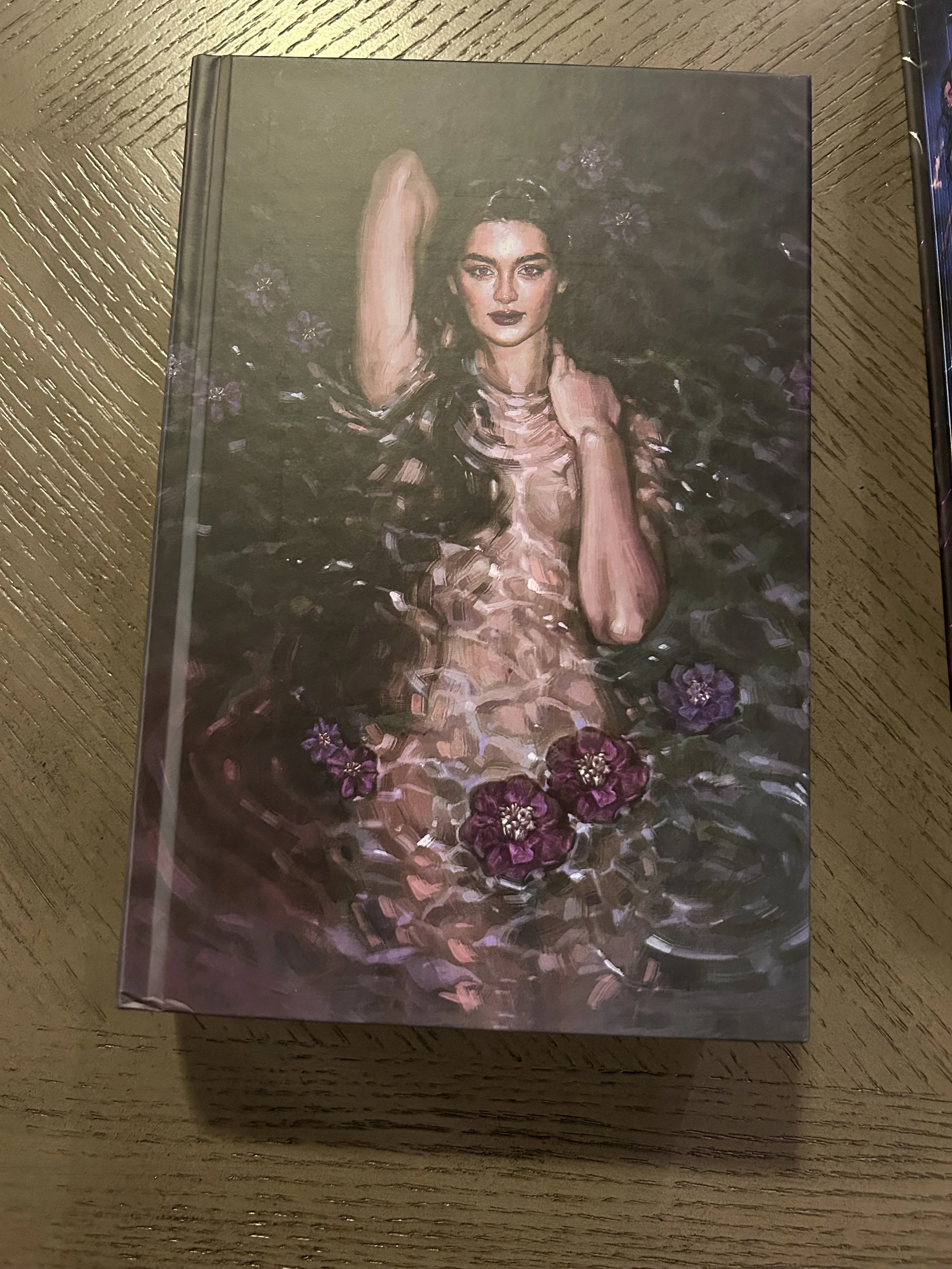 The illustrated retail hardcover of The Poison Daughter showing a woman surrounded by dark water, broken reflections and purple flowers.