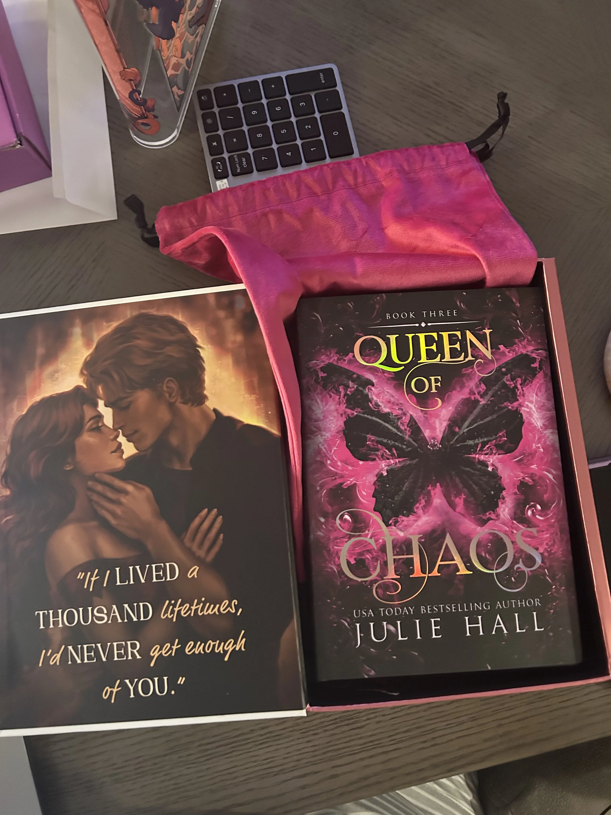 Open Queen of Chaos special-edition box featuring romantic character artwork and a quote beside a bright pink velvet book bag.