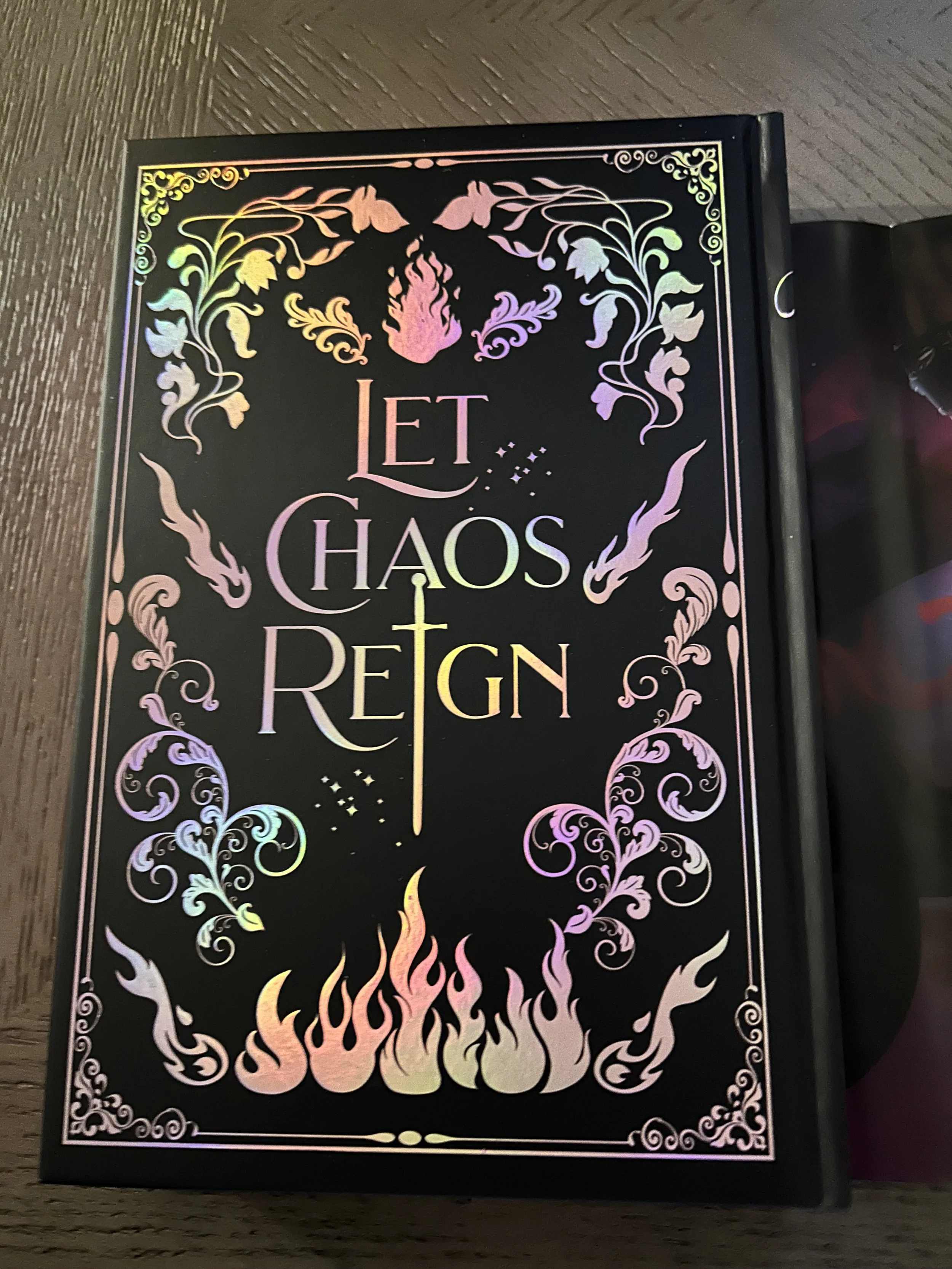 Back of the black Queen of Chaos hardcover with iridescent floral foiling, flames and the words Let Chaos Reign.