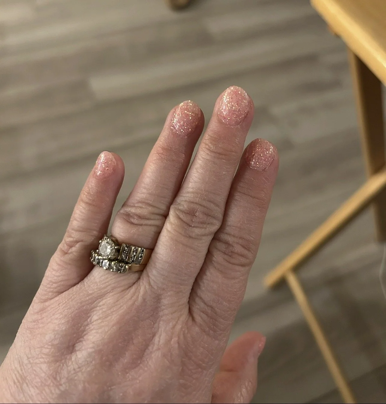 Close-up of sparkly pink manicure with wedding and engagement rings.