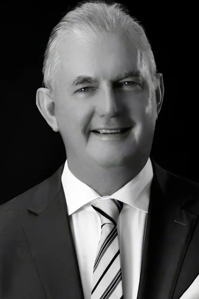 Black and white portrait of a middle-aged man with gray hair in a suit and tie, smiling.