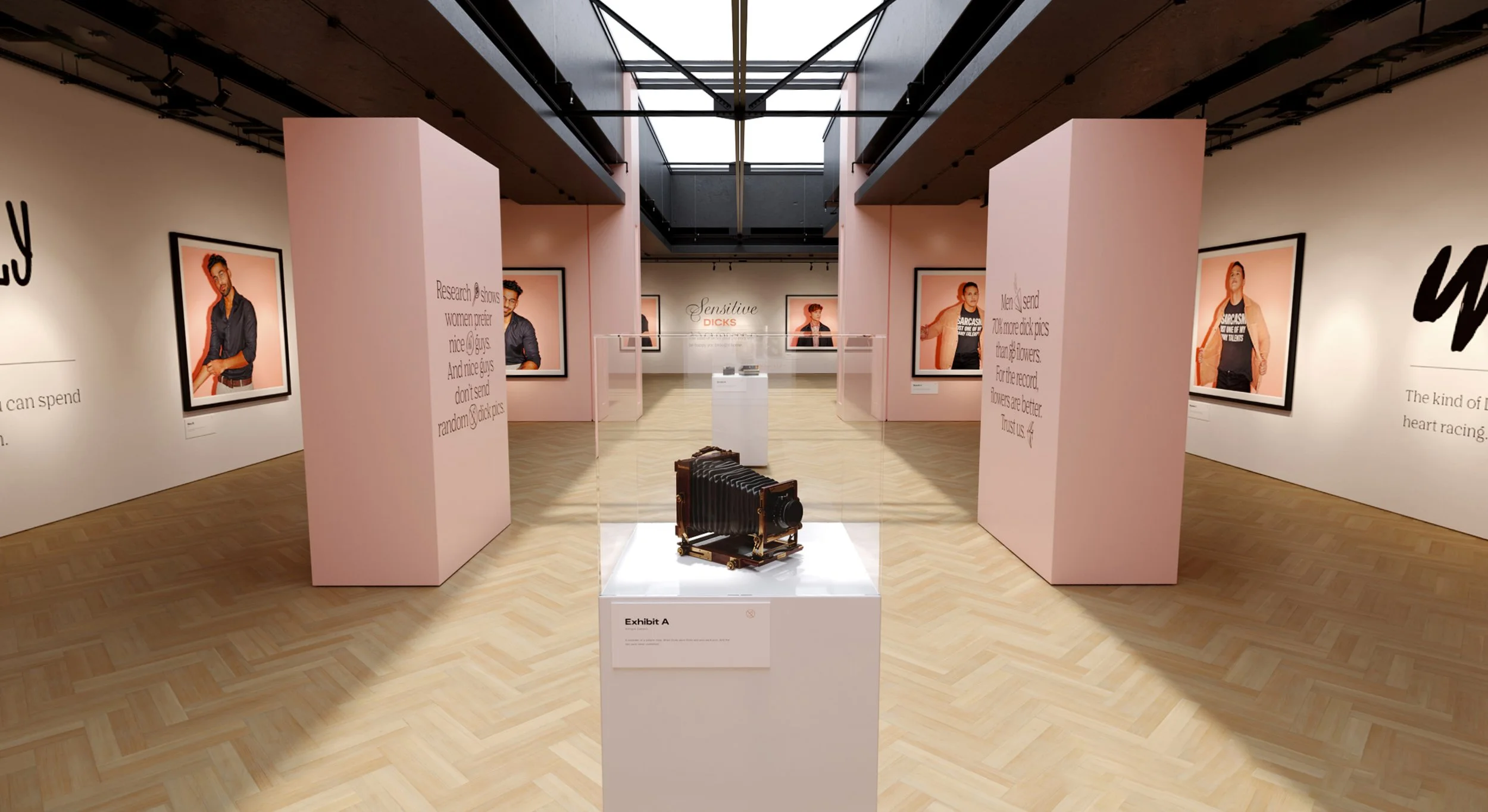 An digital art exhibit in a gallery displaying photos of men on the walls, with a vintage camera on a pedestal in the center and pink display panels. The gallery has wooden floors and a skylight ceiling.