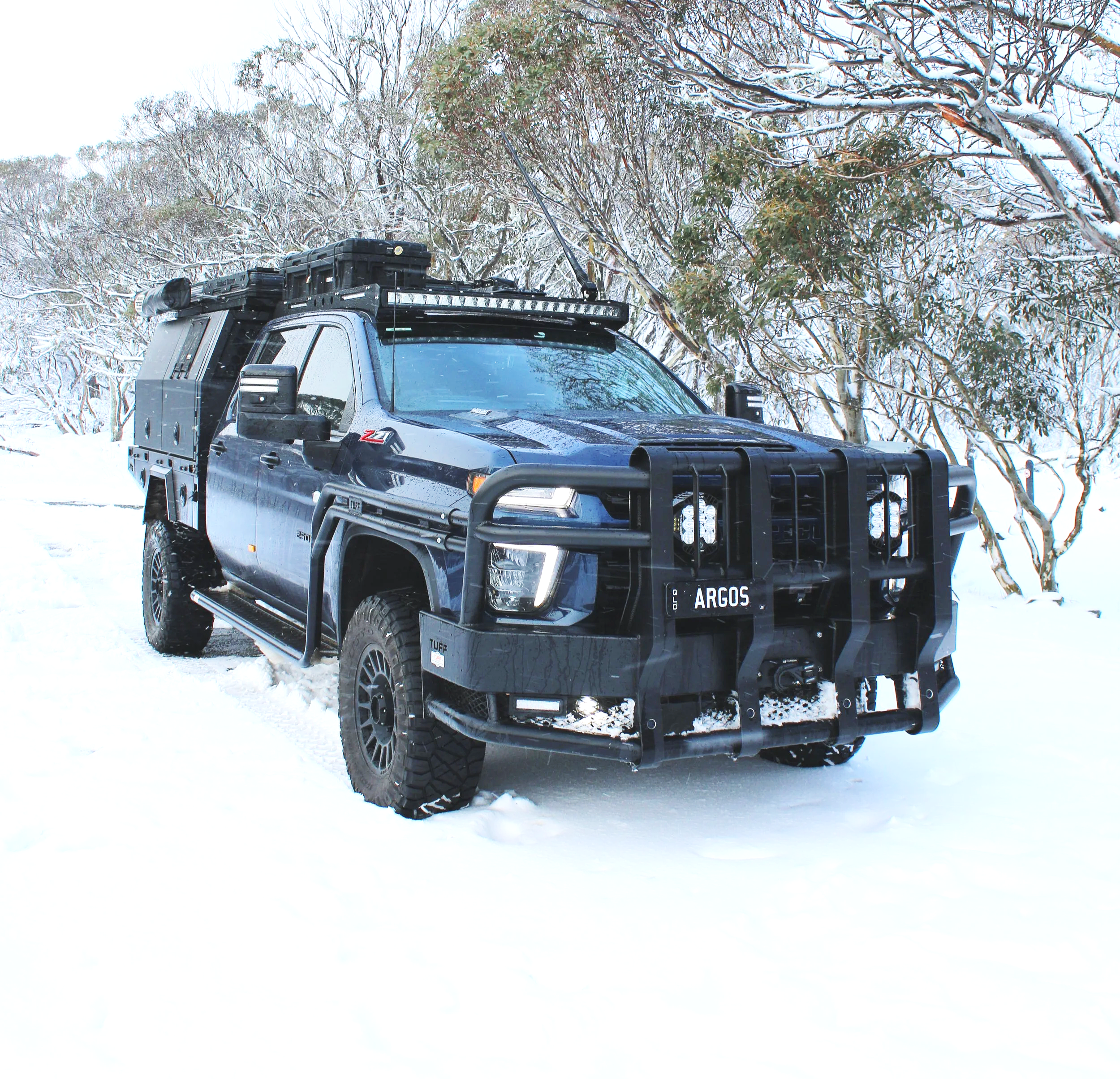 A gray off-road vehicle parked in a snowy landscape with snow-covered trees surrounding it.