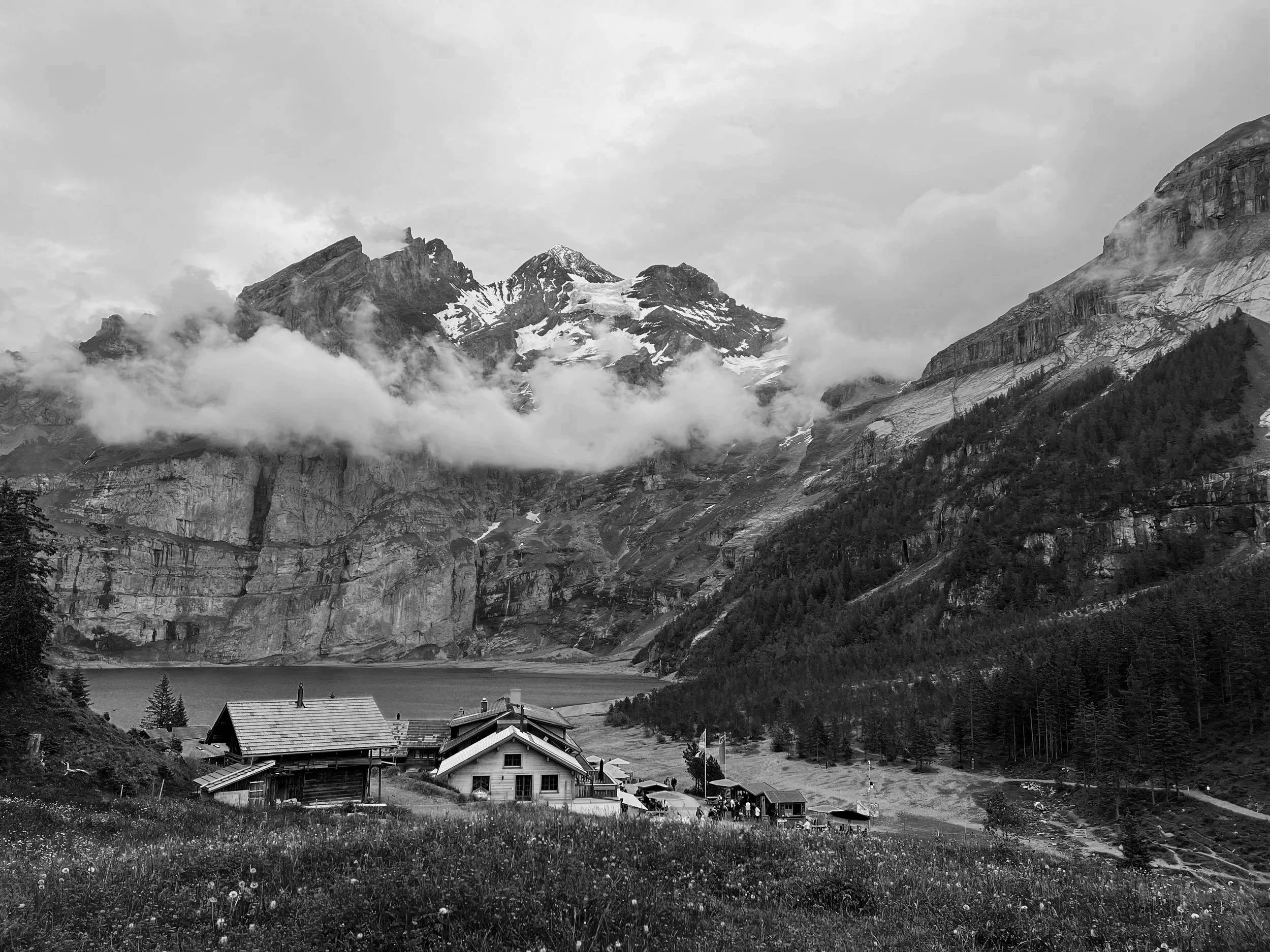 Un village au bord d'un lac entouré de montagnes avec des sommets enneigés, dans une ambiance de montagnes alpines.