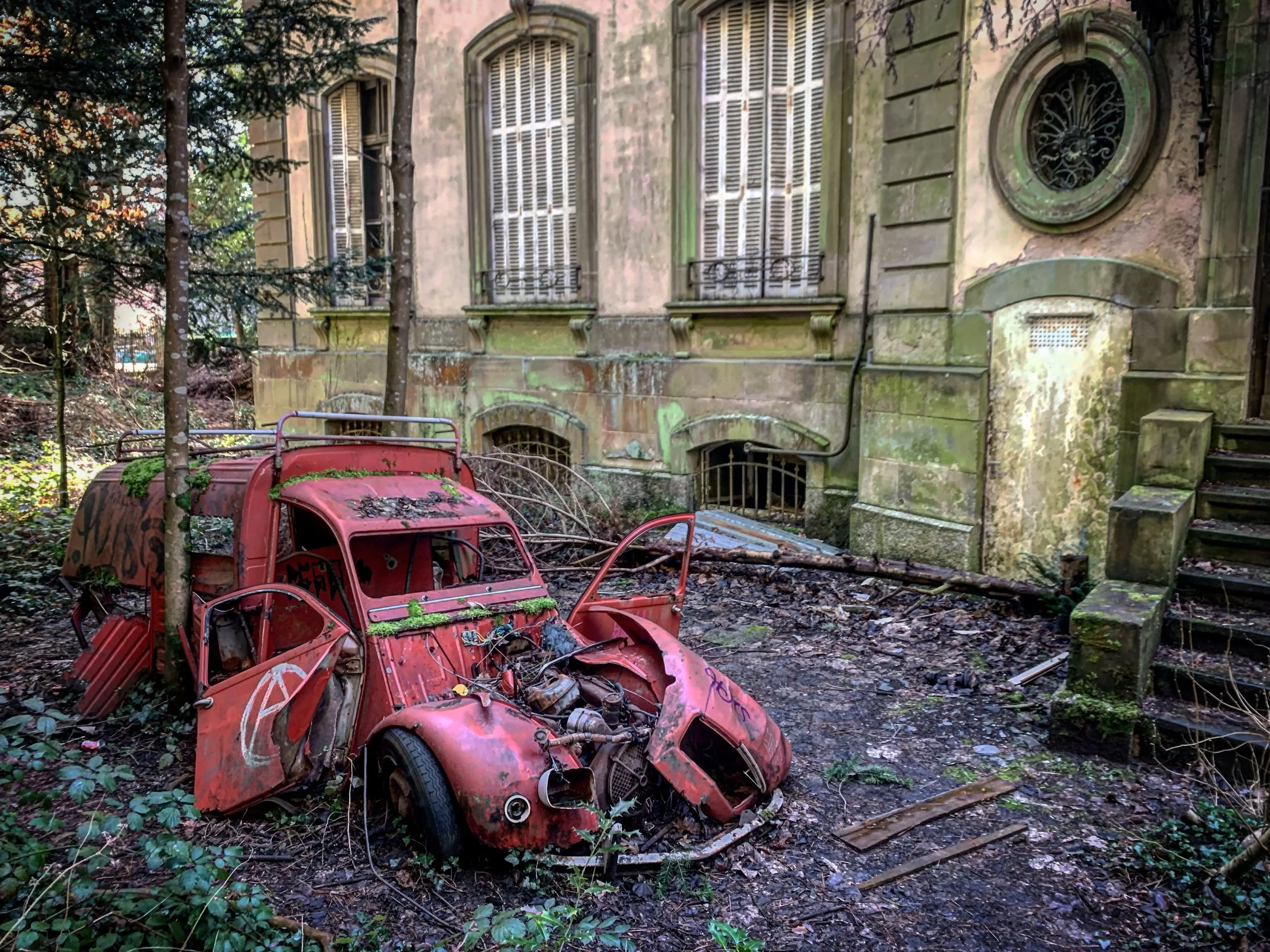 Voiture rouge abandonnée devant un ancien bâtiment en pierre