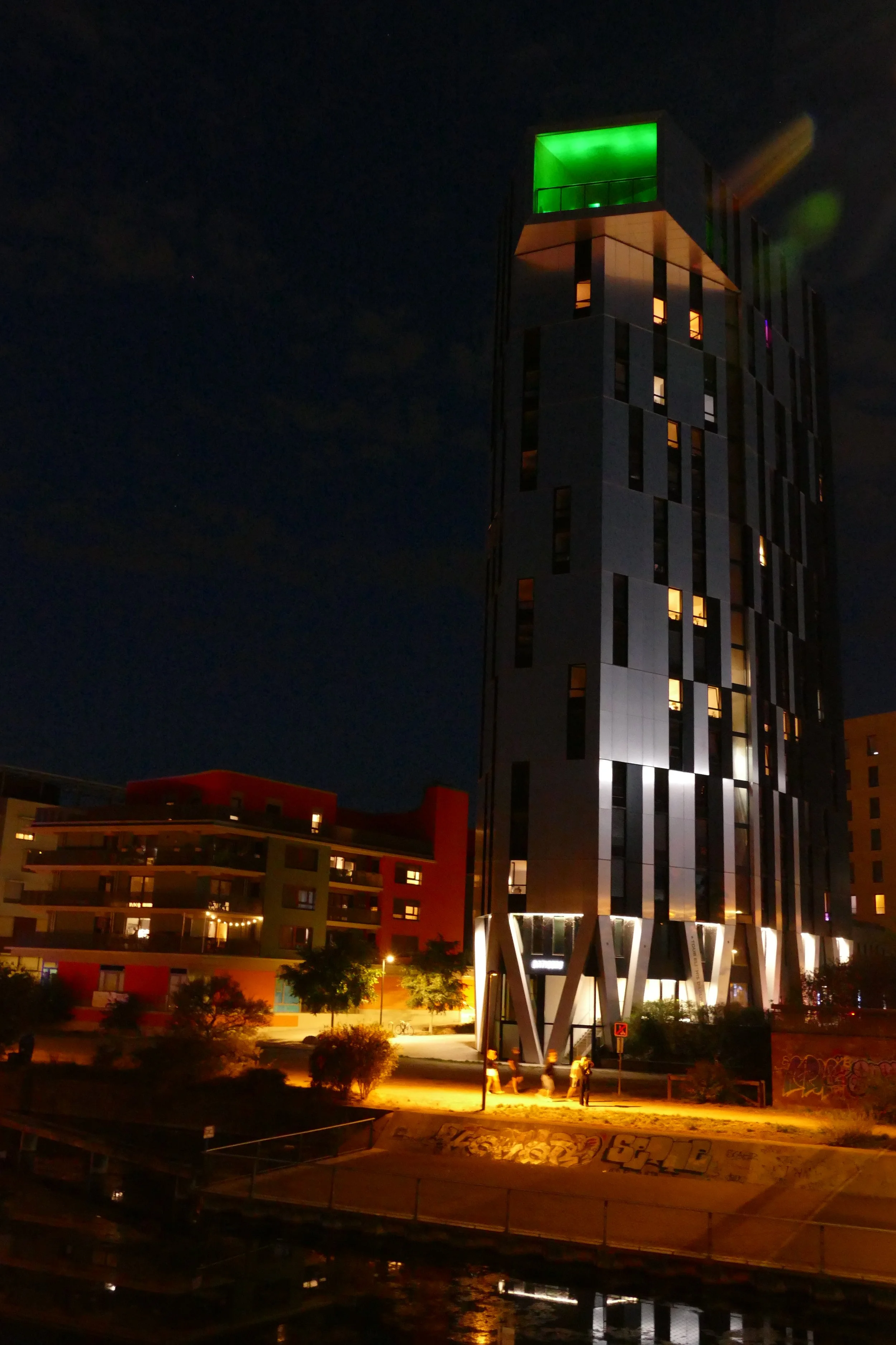 Photographie de Strasbourg la nuit montrant un bâtiment contemporain éclairé par des lumières jaunes, avec des arbres et une façade en briques.
