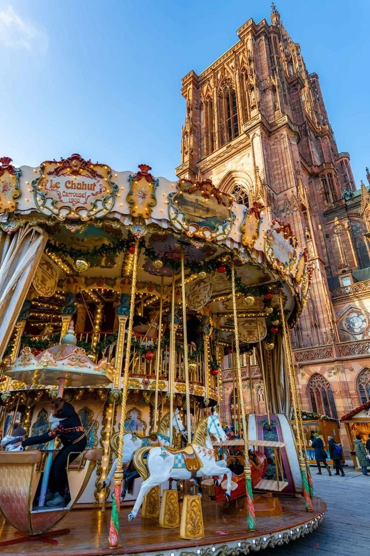 Manège de Noël avec chevaux en bois colorés devant une vieille cathédrale gothique.