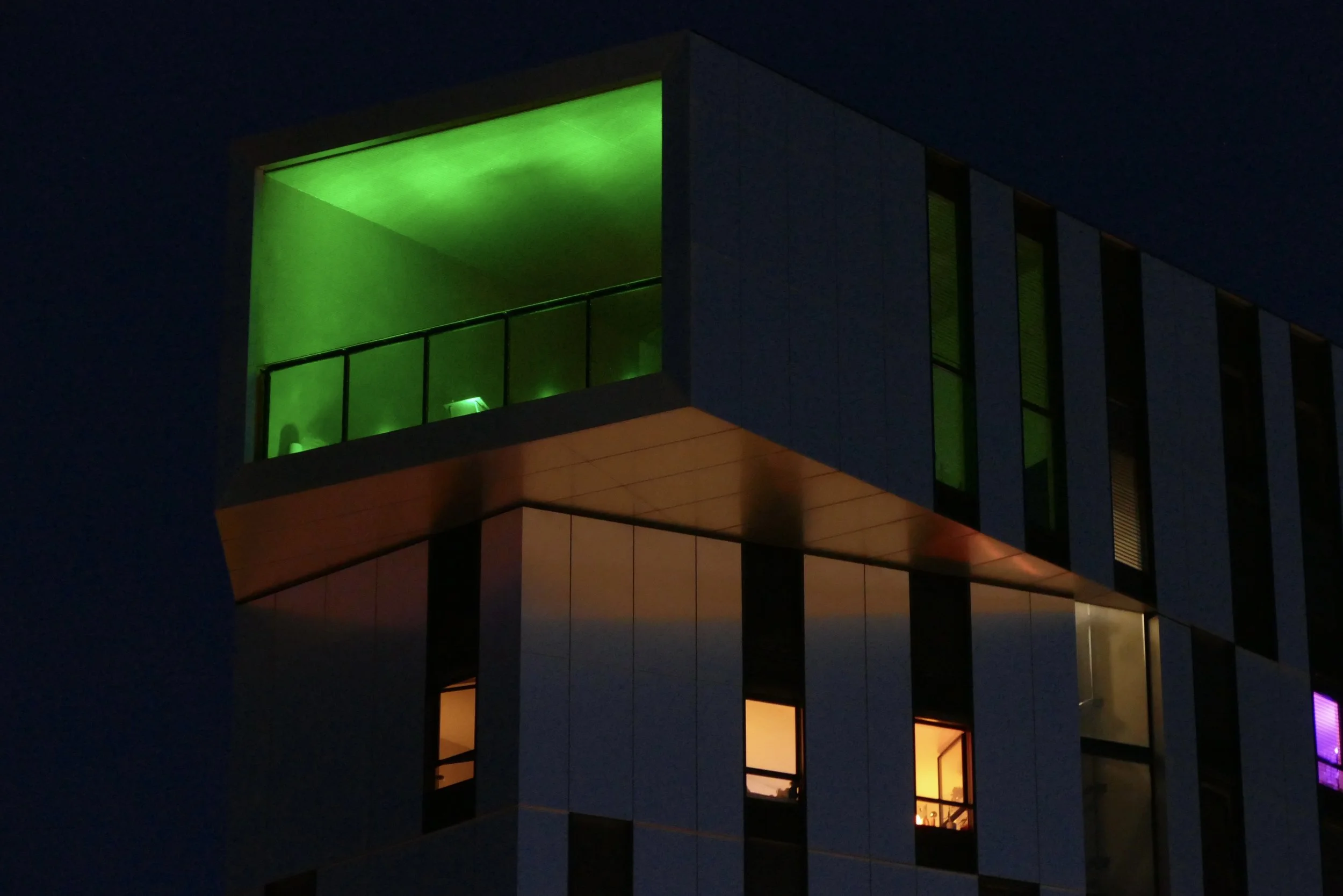 Photographie d'un bâtiment contemporain à Strasbourg éclairé de nuit par des lumières vertes, violettes et orange.