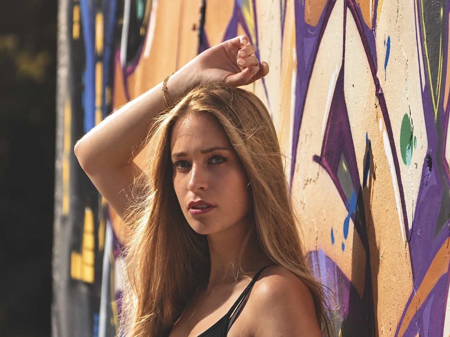 Jeune femme aux cheveux bruns devant un mur de graffitis colorés.