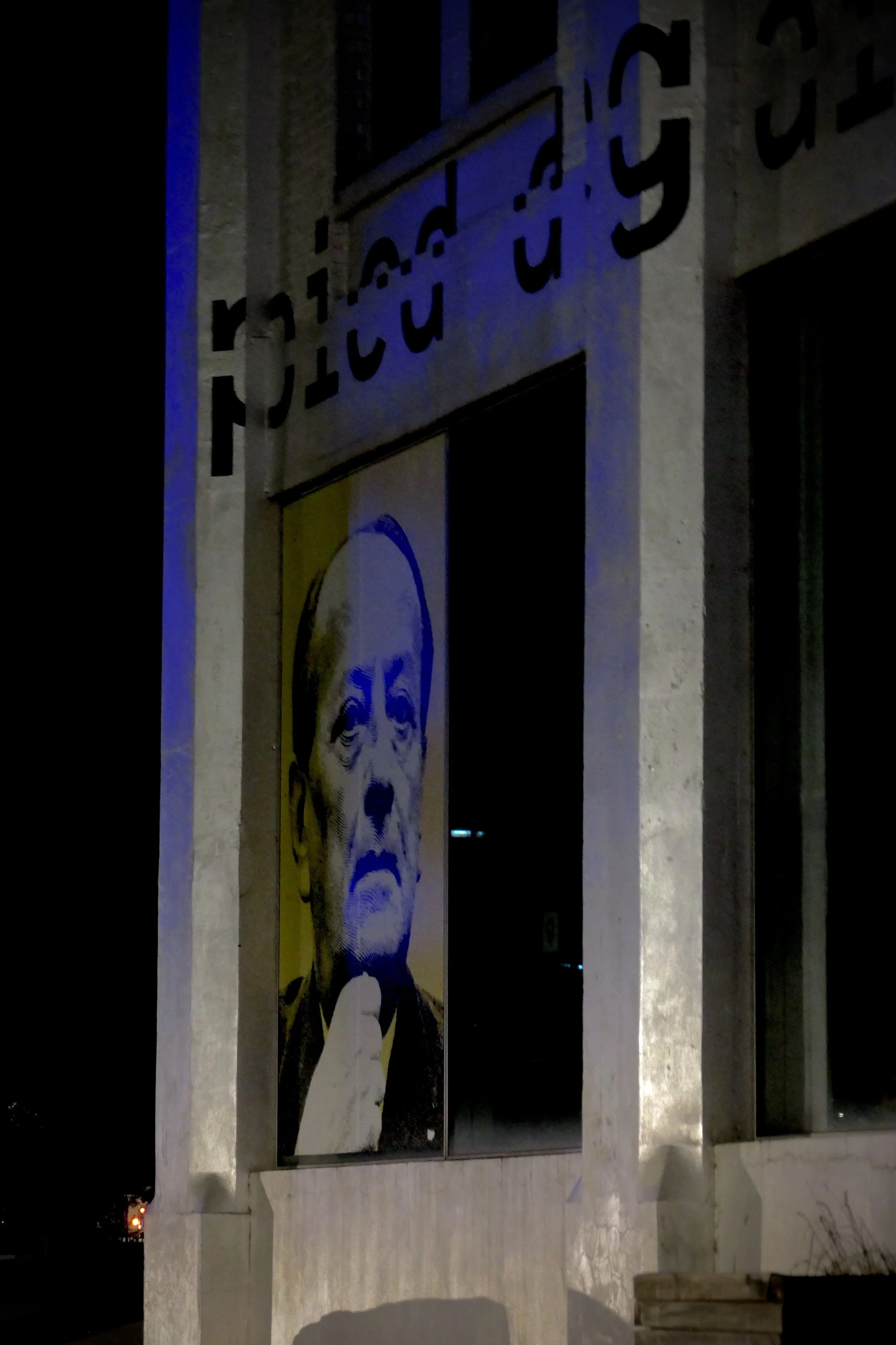 Photographie nocturne à Strasbourg d'une œuvre artistique représentant un visage sur la façade d'un bâtiment.