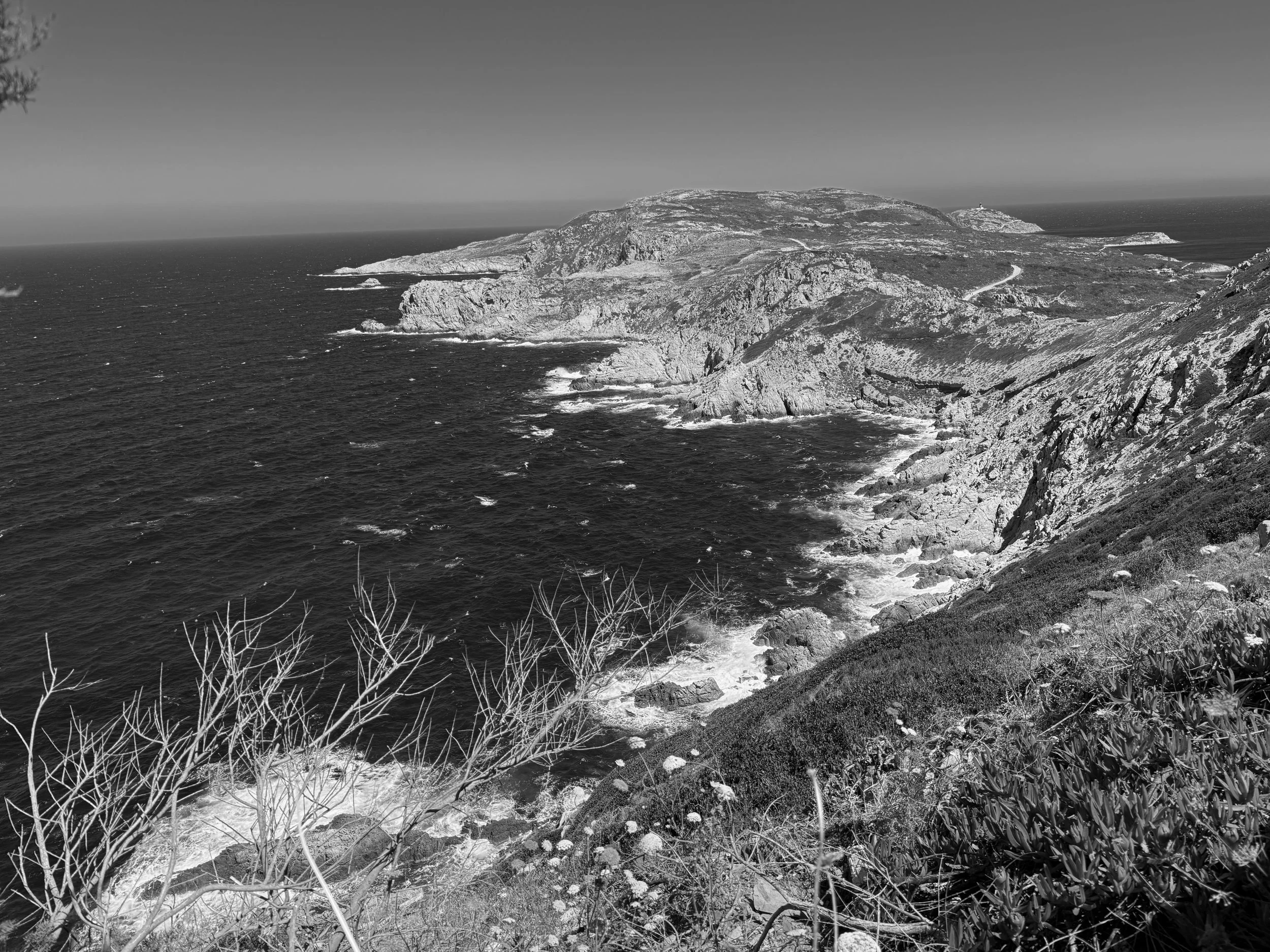 Paysage côtier rocheux avec des falaises, l'océan en avant et un phare au loin sur une colline.