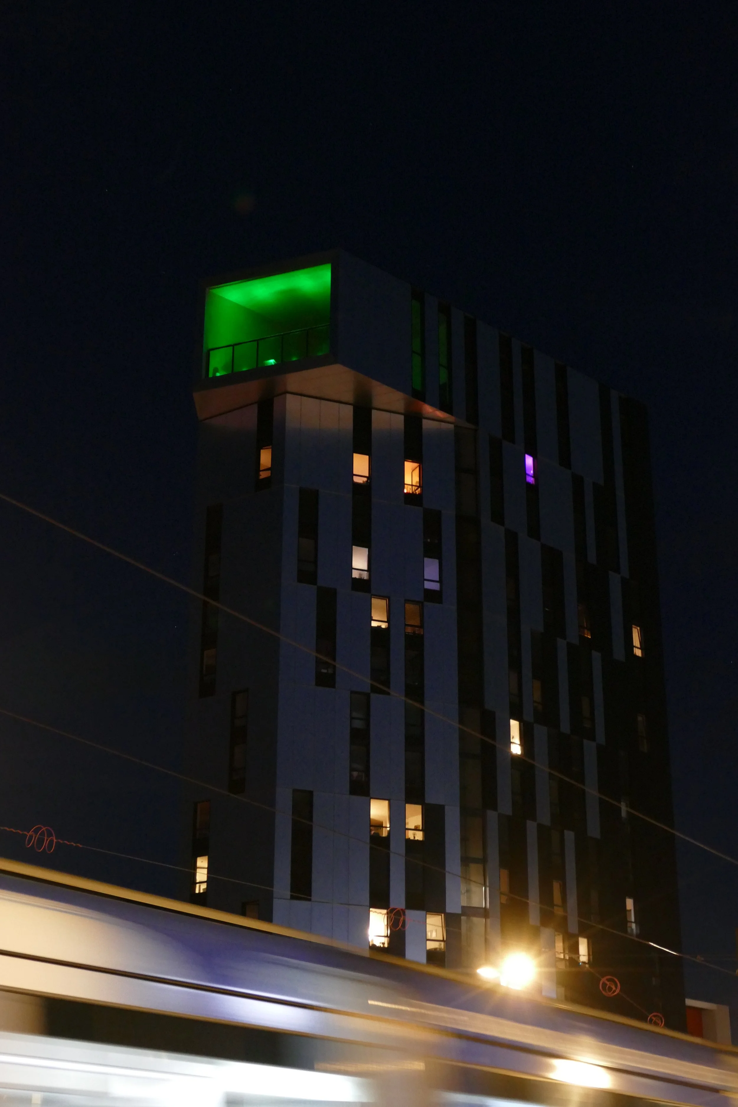 Photographie de Strasbourg de nuit montrant un bâtiment moderne aux fenêtres éclairées et un balcon illuminé en vert.