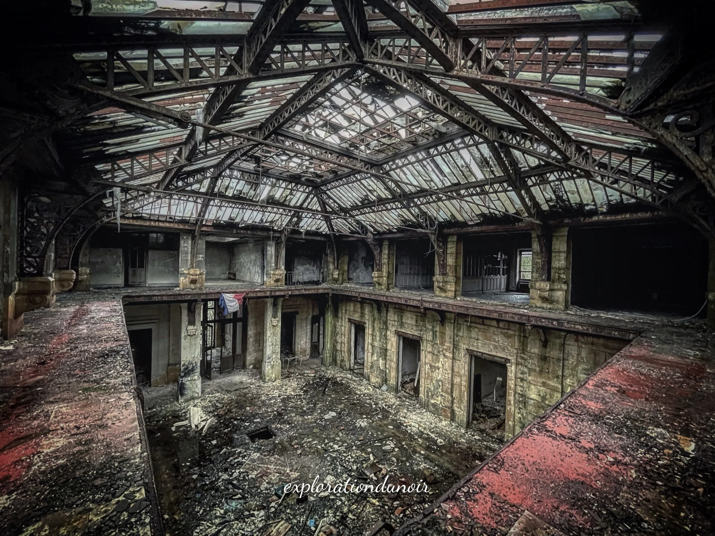 Salle abandonnée avec plafond en verre brisé et structures métalliques