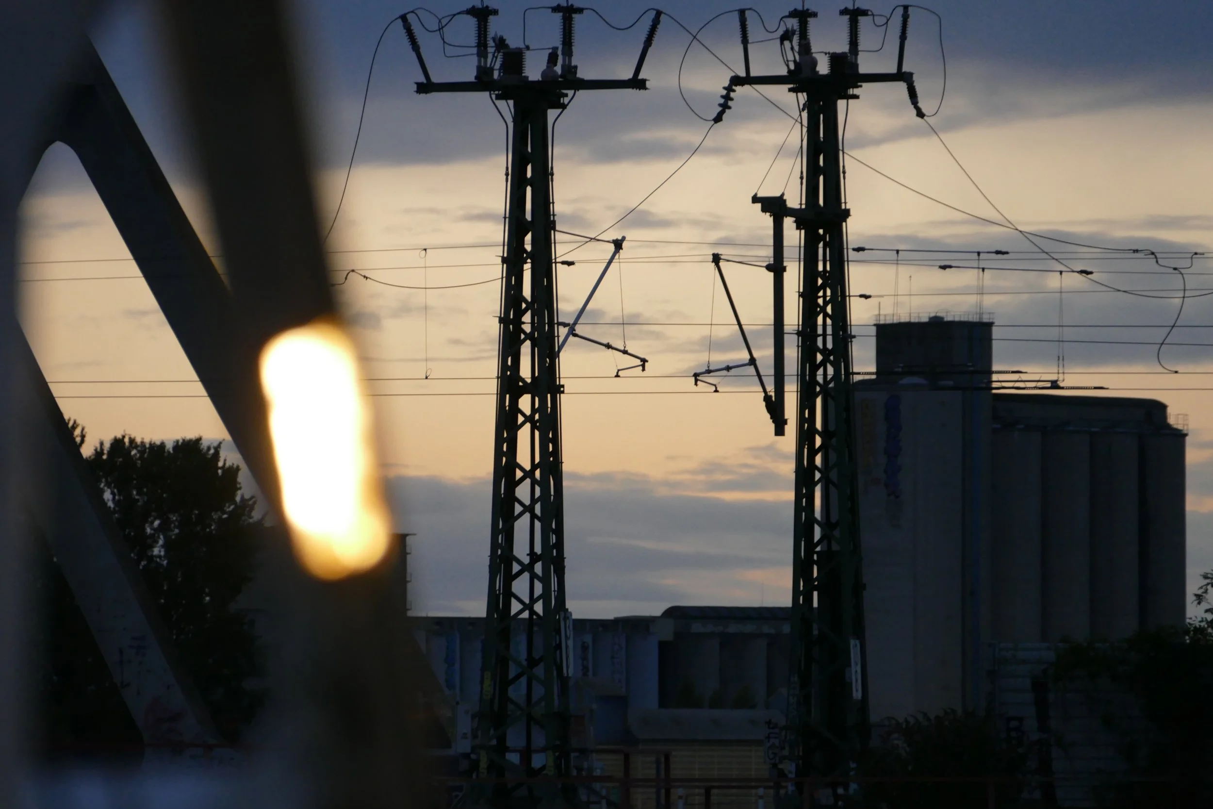 Poteaux électriques avec câbles électriques contre un ciel au coucher du soleil, avec des nuages gris.