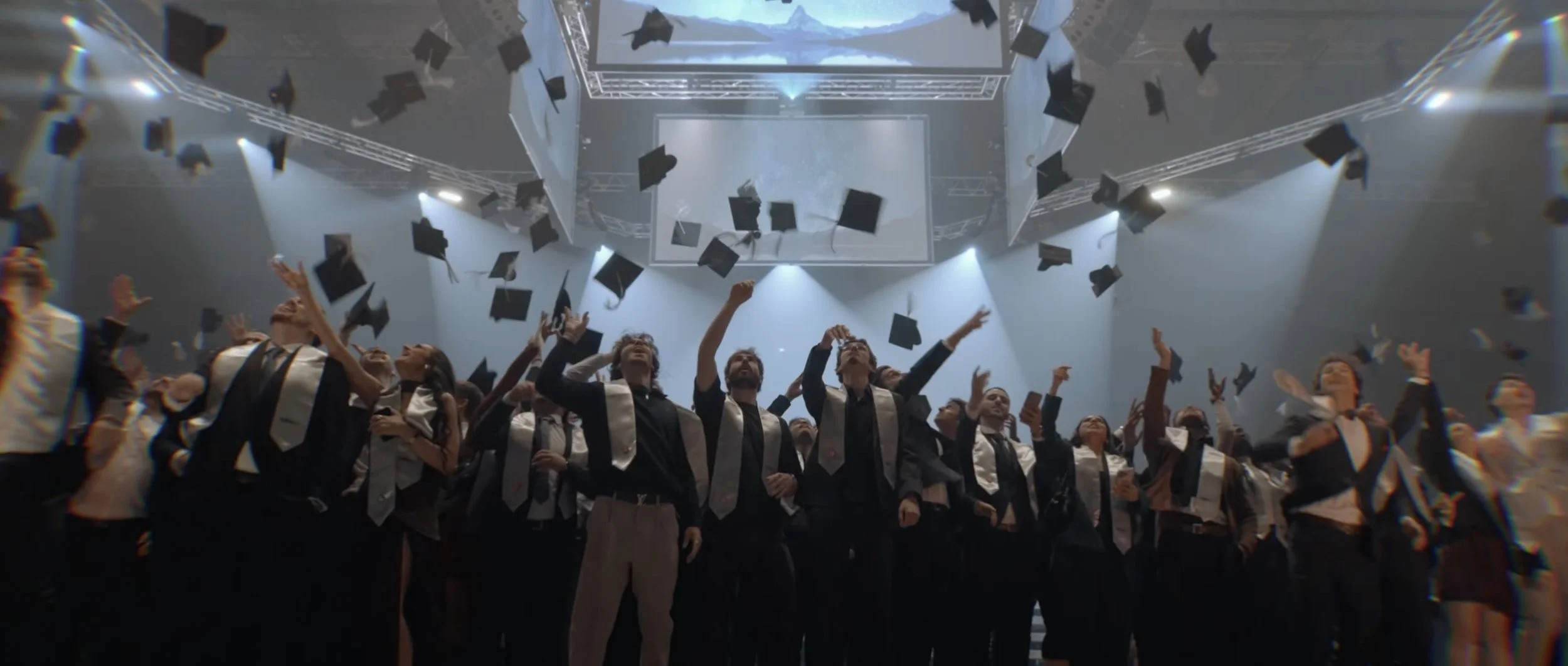 Groupe de diplômés en robe et toges lançant leurs chapeaux en l'air lors d'une cérémonie de remise de diplômes dans une salle bien éclairée.