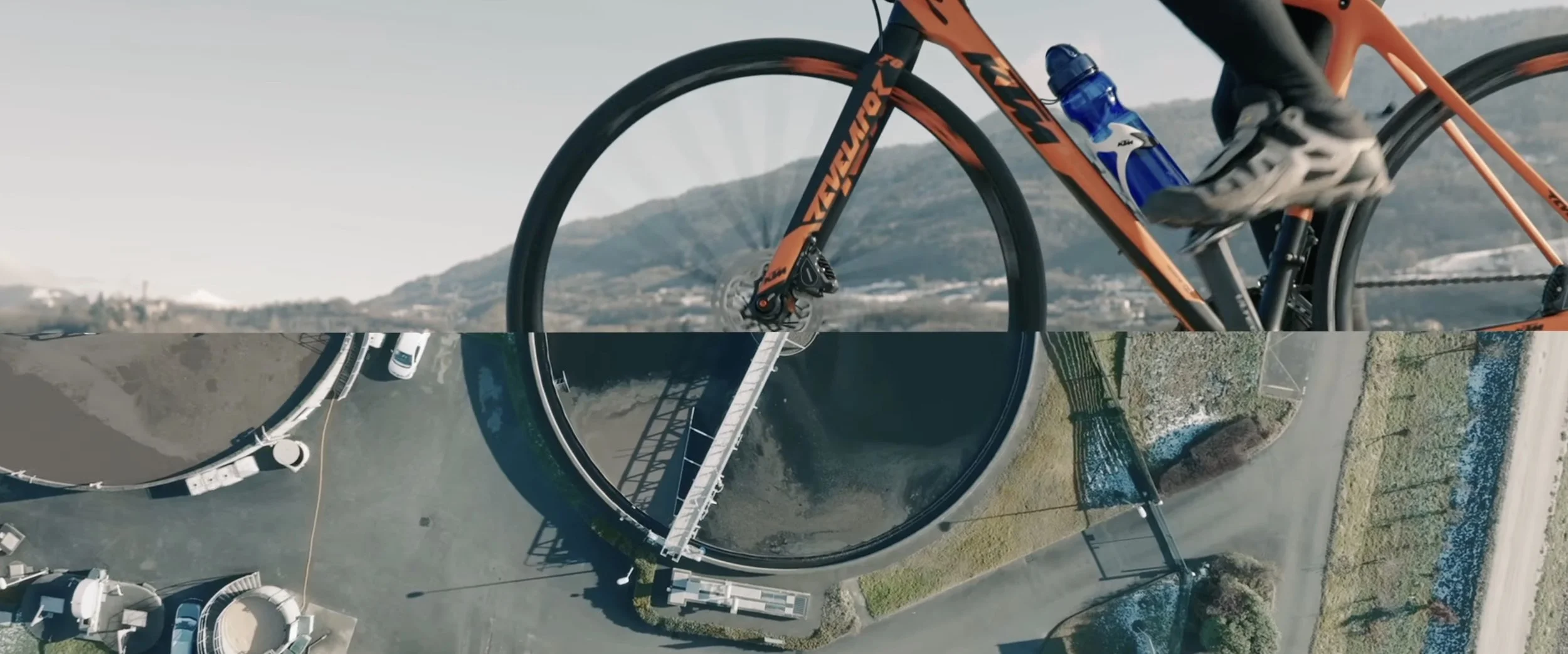 Une image d'un vélo de course orange avec un cadre de marque KTM, placé sur un terrain en plein air avec des collines en arrière-plan. La moitié inférieure de l'image présente une vue aérienne d'une piscine avec un toboggan et des voitures garées à proximité.