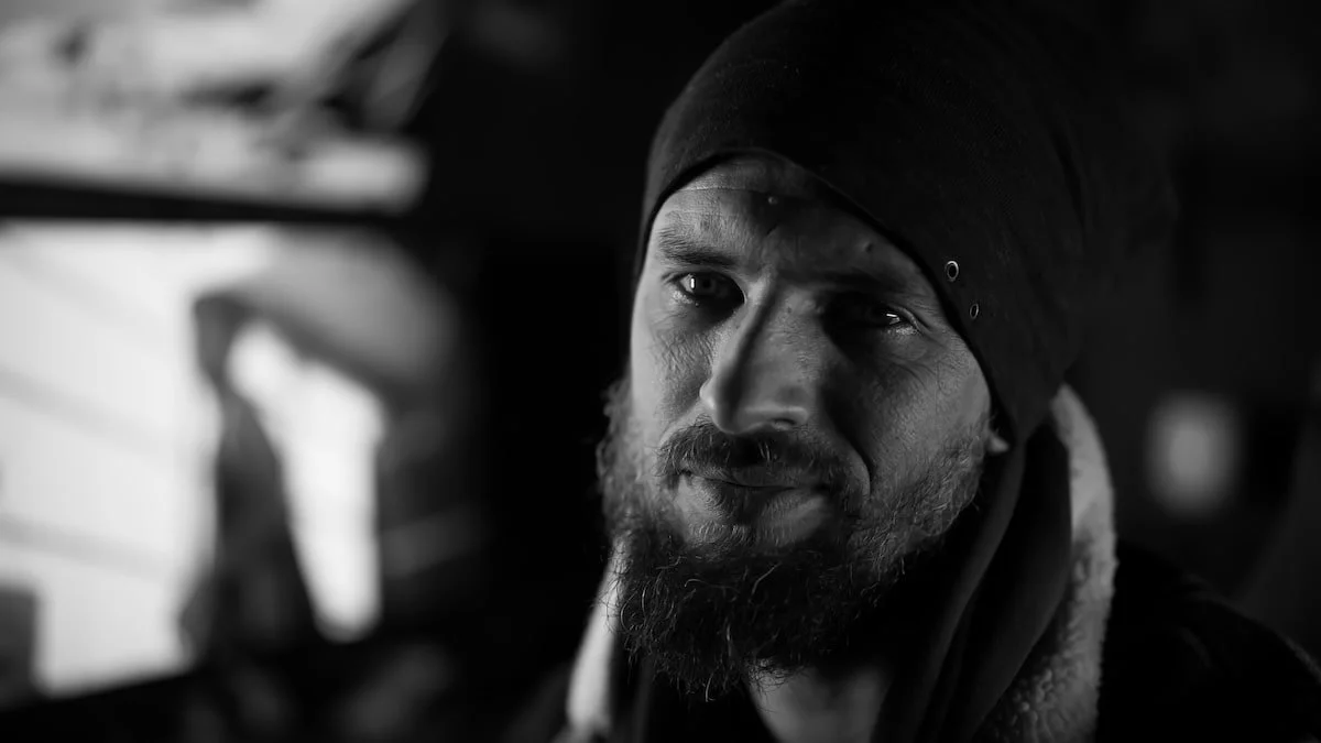 Portrait en noir et blanc d'un homme avec une barbe, portant un bonnet noir, regardant vers la caméra.