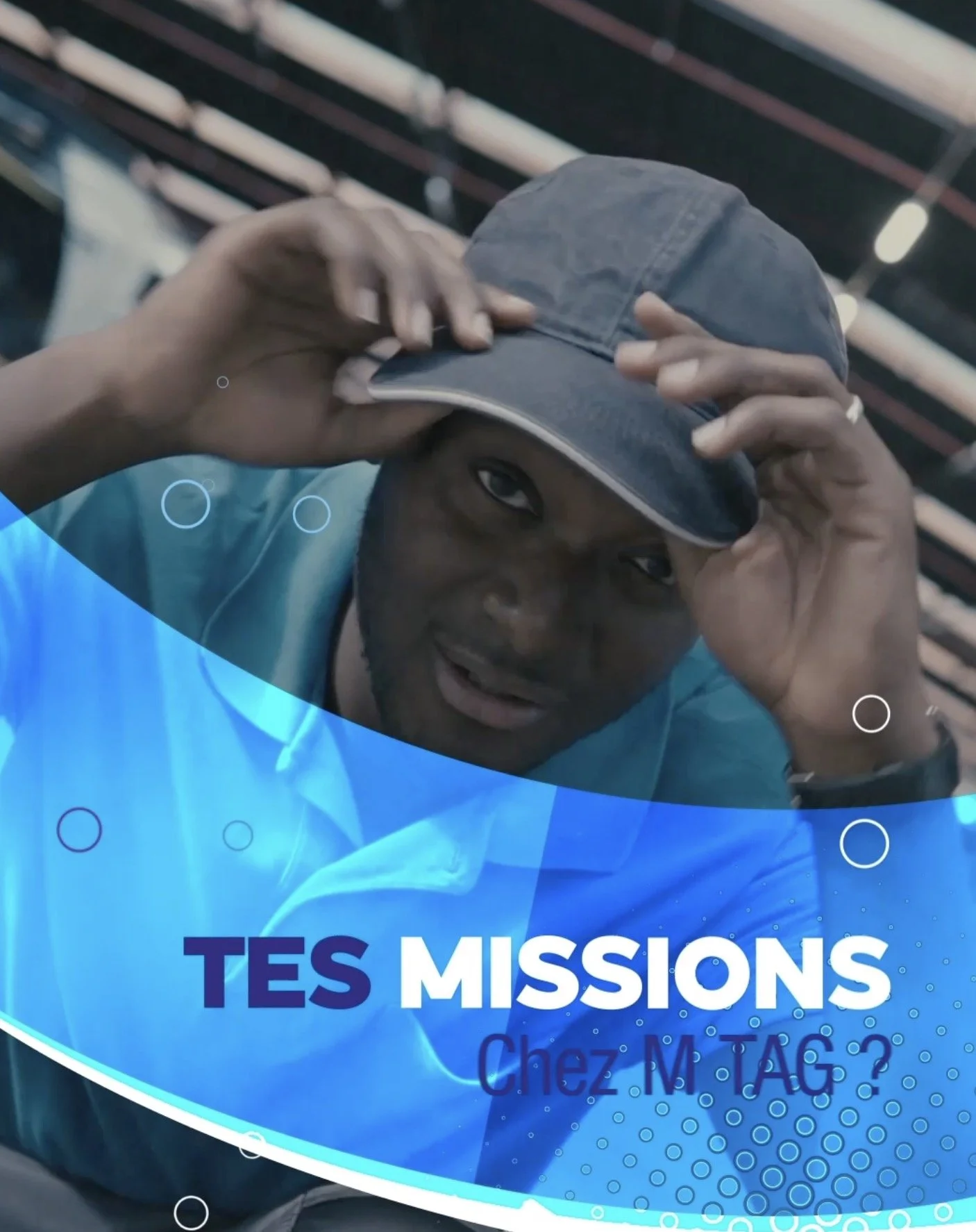 Une personne porte une casquette grise et regarde la caméra, avec un fond d'une structure en métal et le texte "TES MISSIONS" en français.