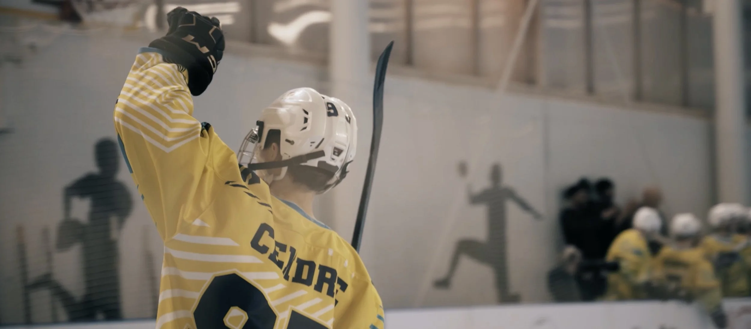 Un joueur de hockey sur glace en uniforme jaune et casque blanc, célébrant un but en levant son bras dans une patinoire.