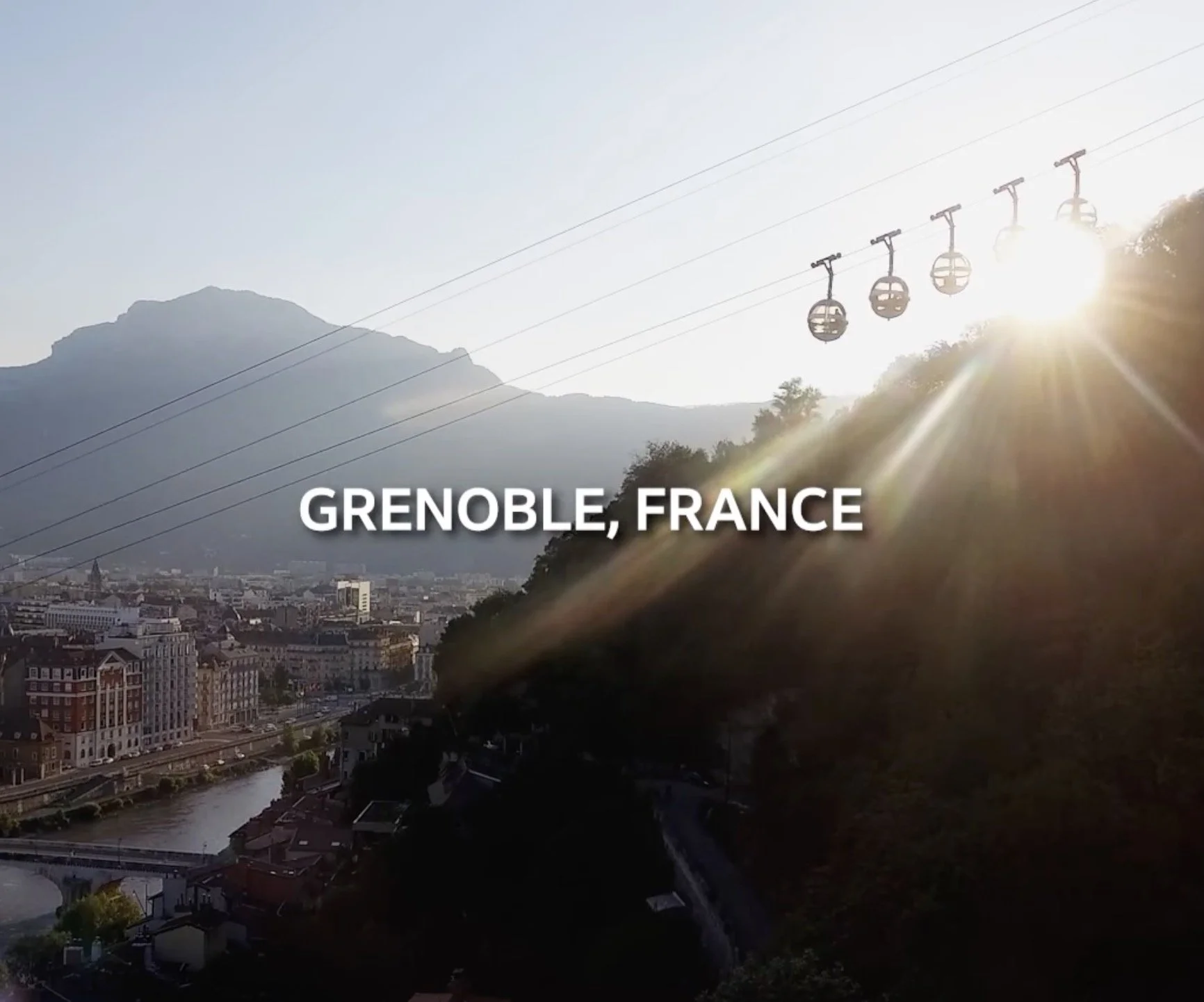 Vue de la ville de Grenoble en France avec la montagne en arrière-plan et un téléphérique avec des cabines suspendues sous le soleil couchant.