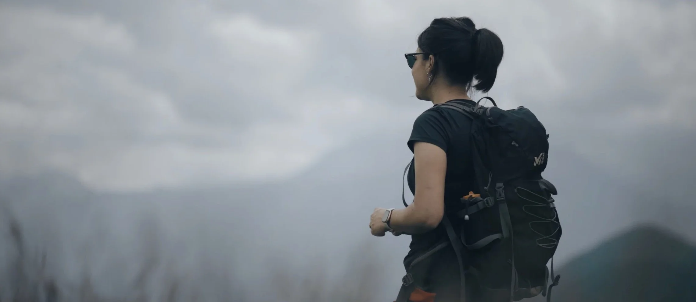 Femme qui marche avec un sac à dos dans un paysage nuageux.