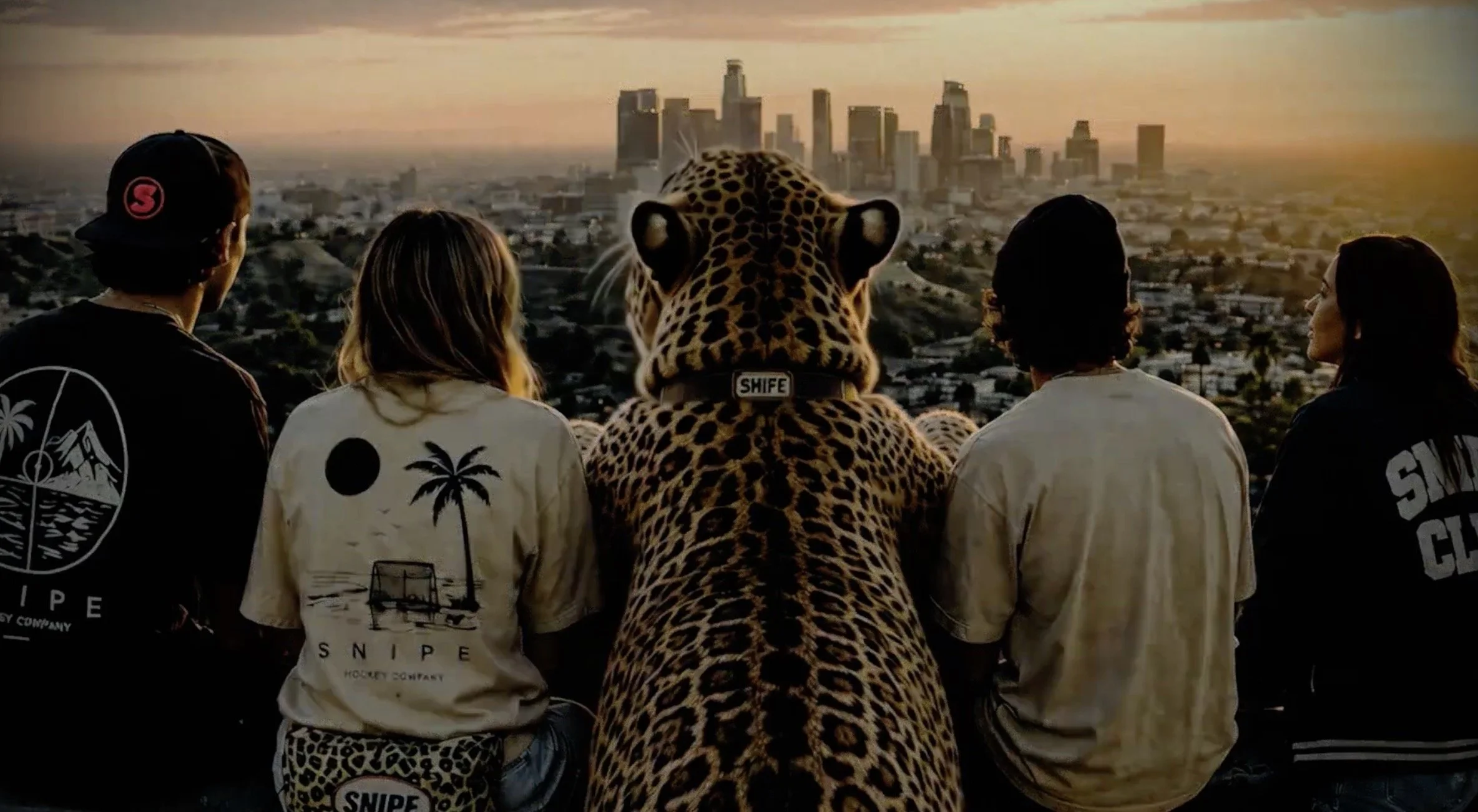 Groupe de cinq personnes portant des vêtements avec des motifs de palmier, avec en leur centre une personne en costume de léopard, regardant vers la ville de Los Angeles au coucher du soleil.